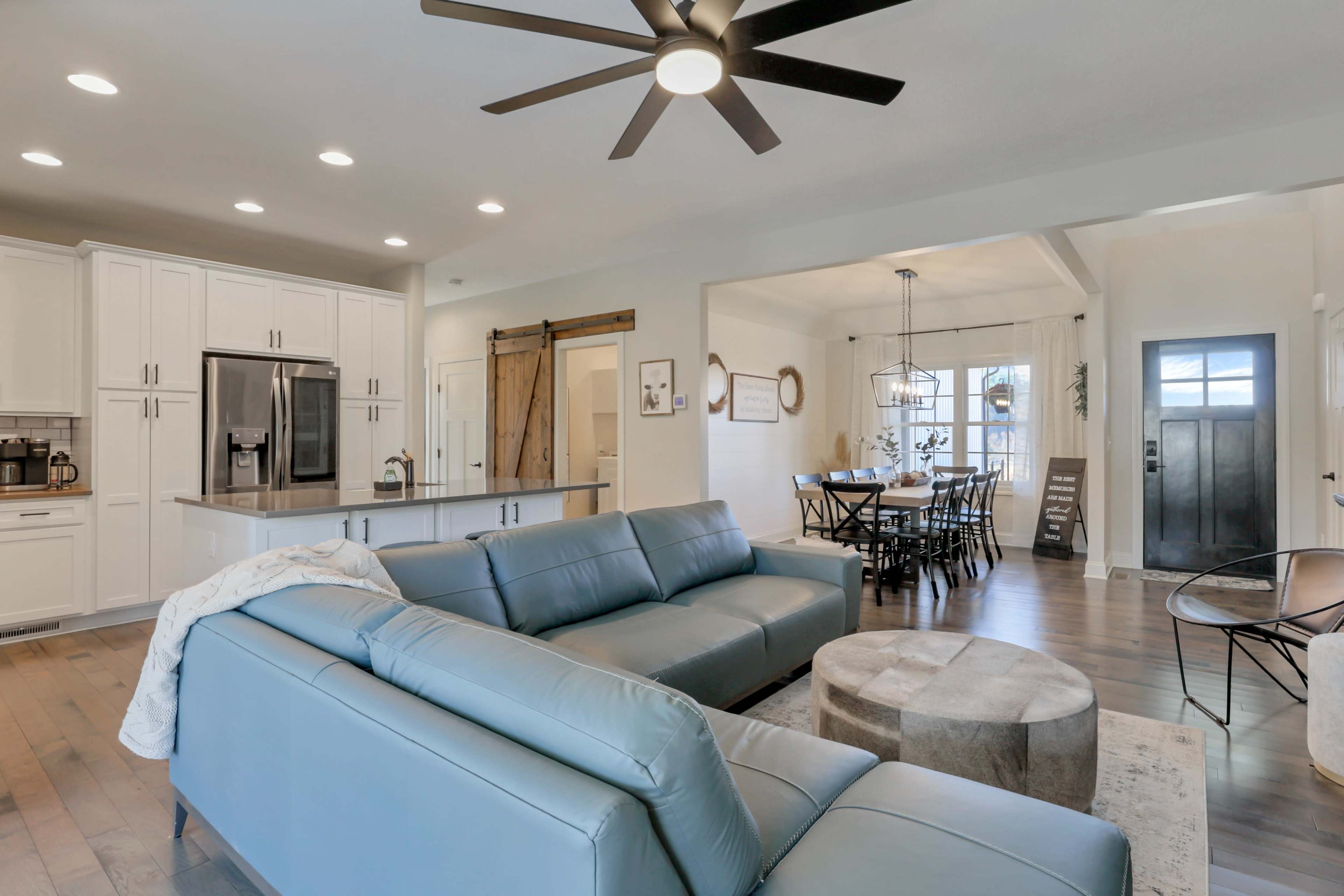 A spacious living area featuring a blue sectional sofa, a round coffee table, and a dining space with a large table and chair set under a pendant light.