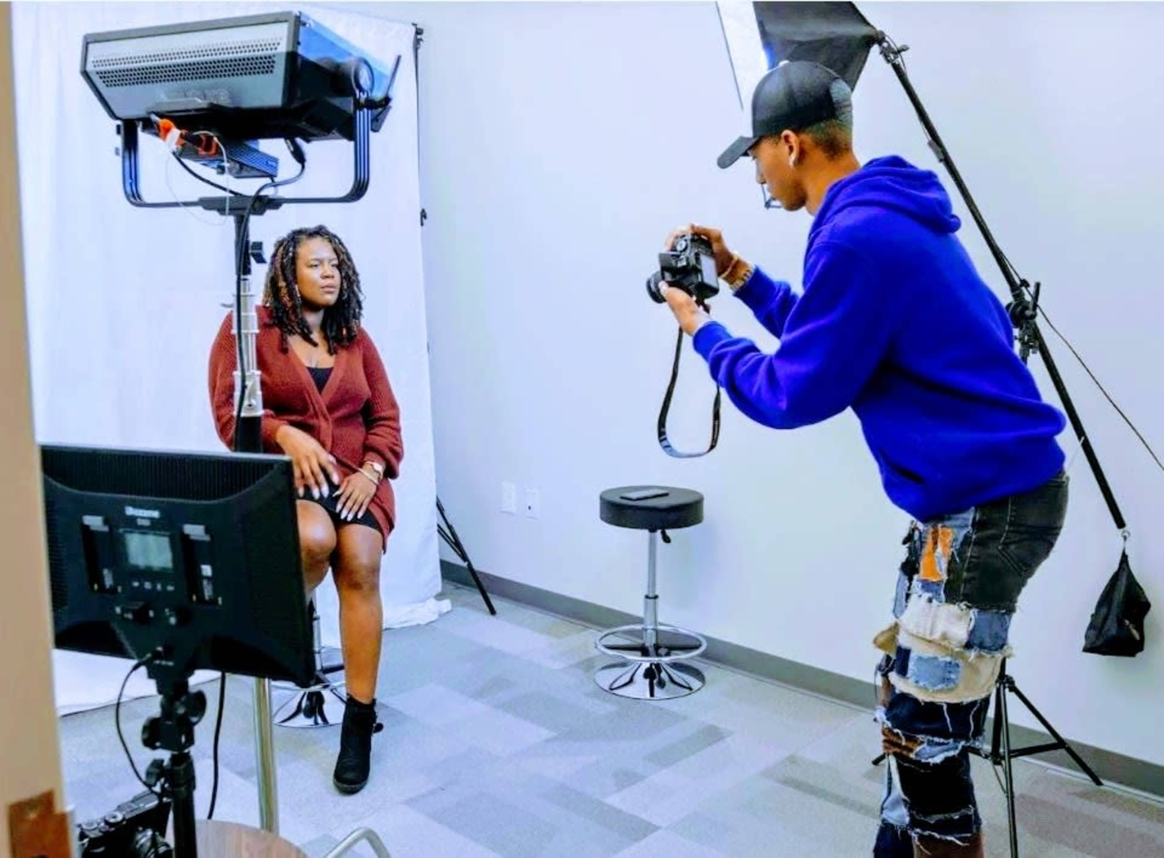 A photographer is capturing a portrait of a woman seated in a studio setting with professional lighting and backdrops.