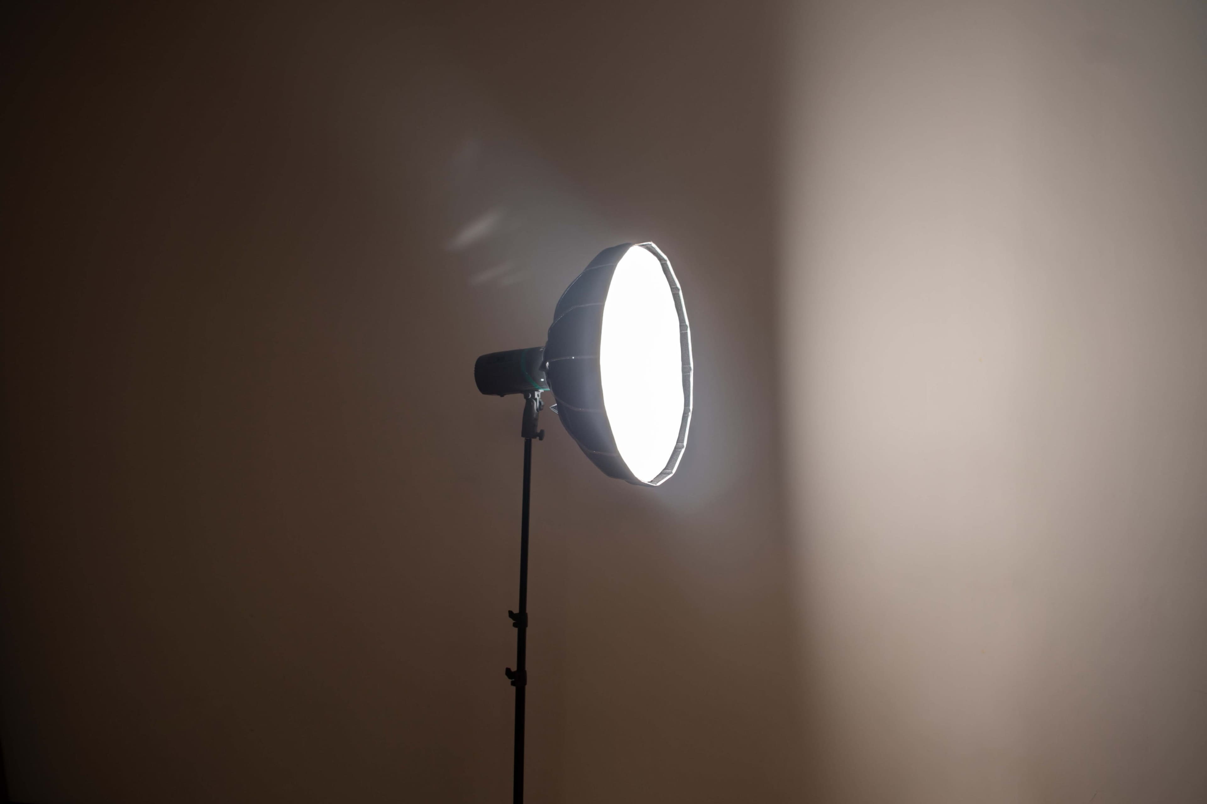 A large circular light source on a stand illuminates a plain wall.