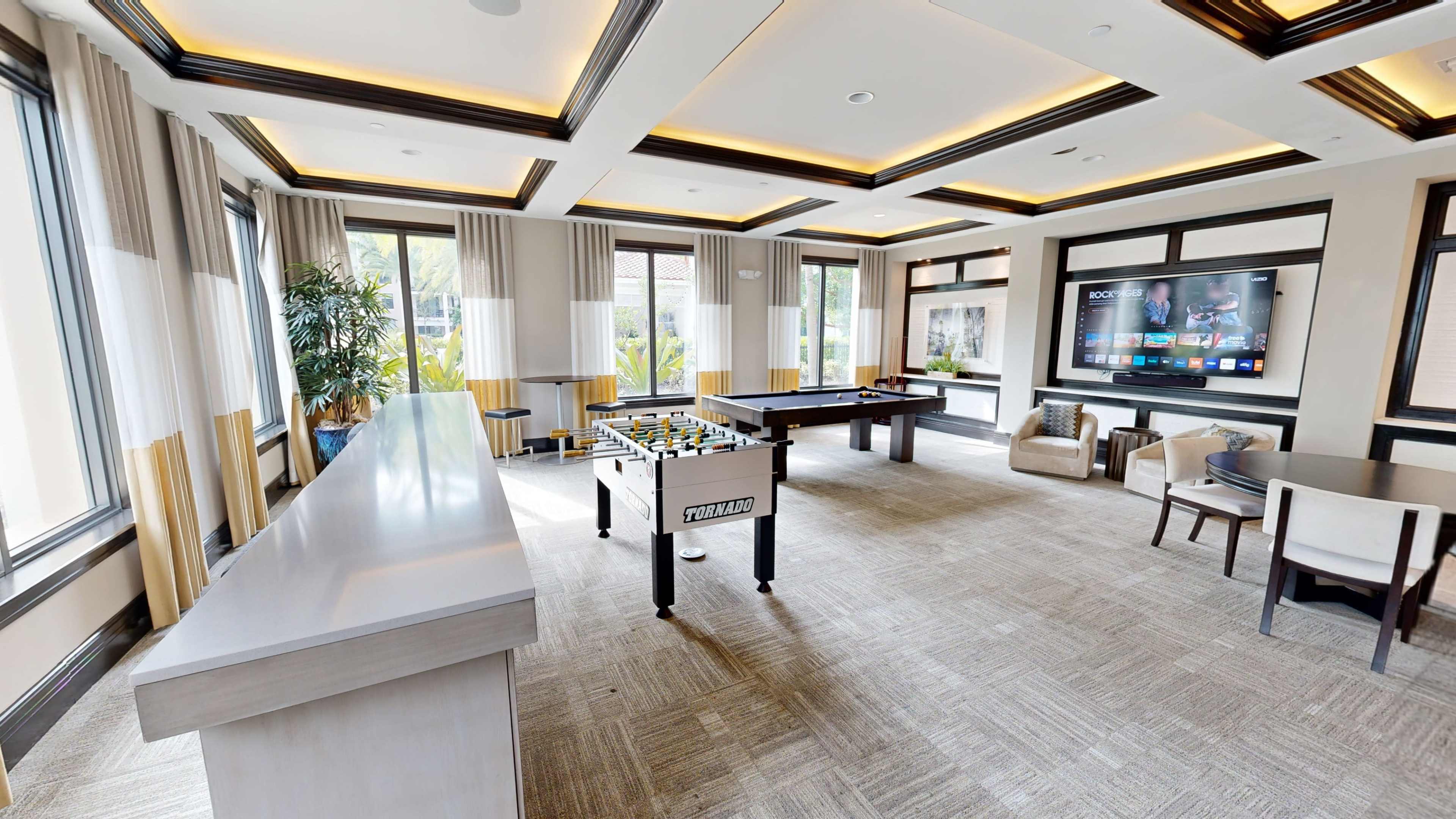 The image shows a spacious game room featuring a foosball table, a pool table, and a large television against the wall.