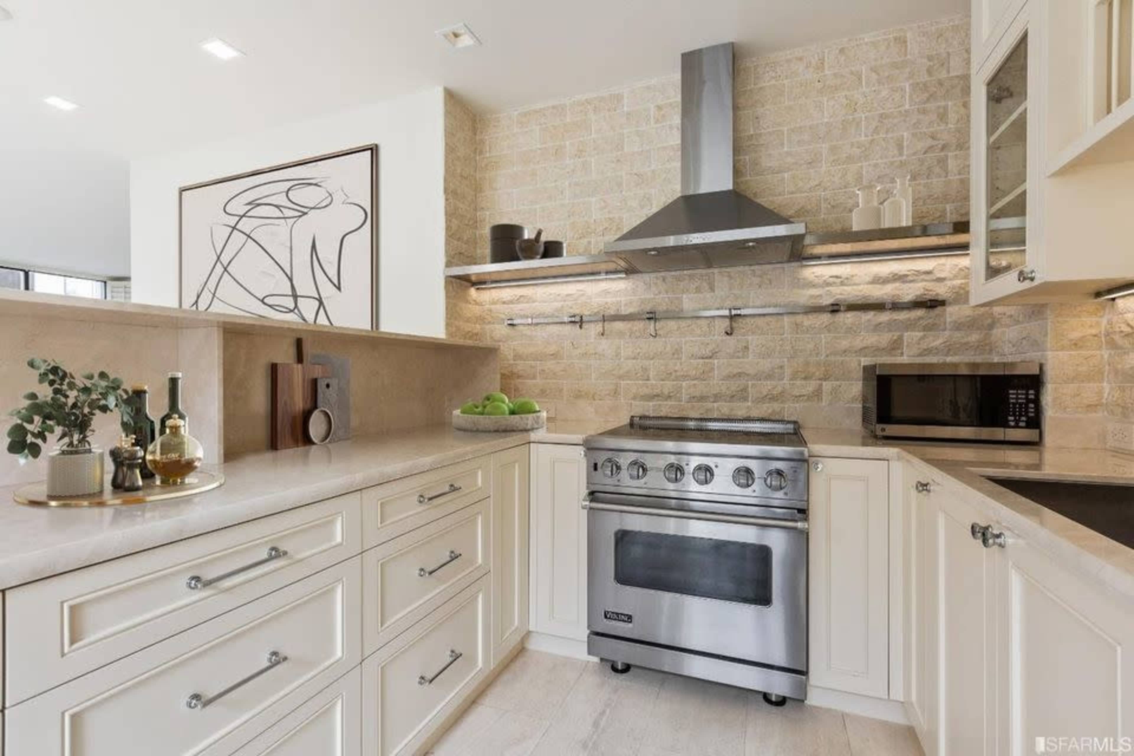 A modern kitchen features light cabinetry, a stainless steel stove, and a stone backsplash with decorative accents.