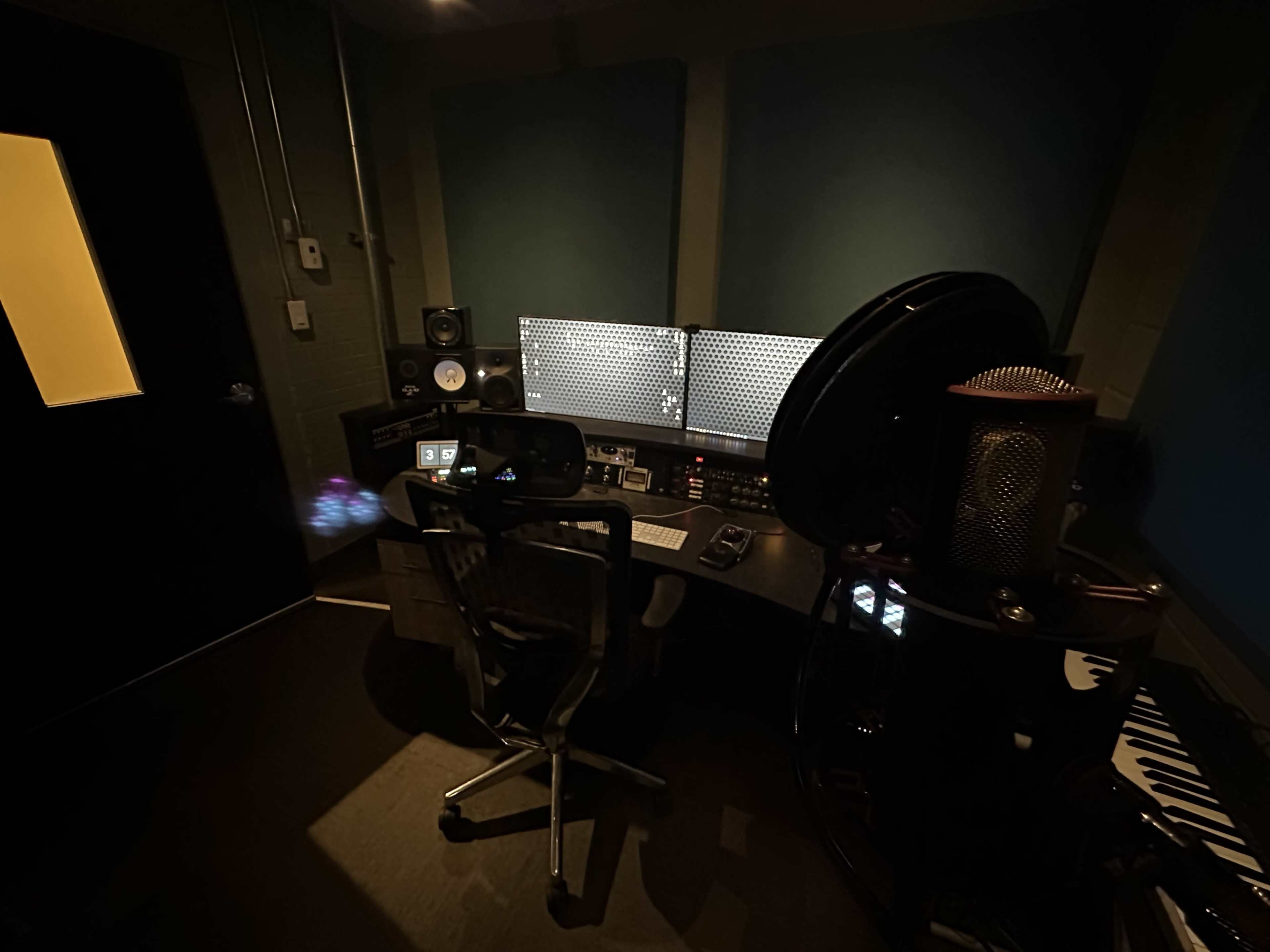 A dimly lit music studio with a large desk equipped with multiple screens and audio equipment.