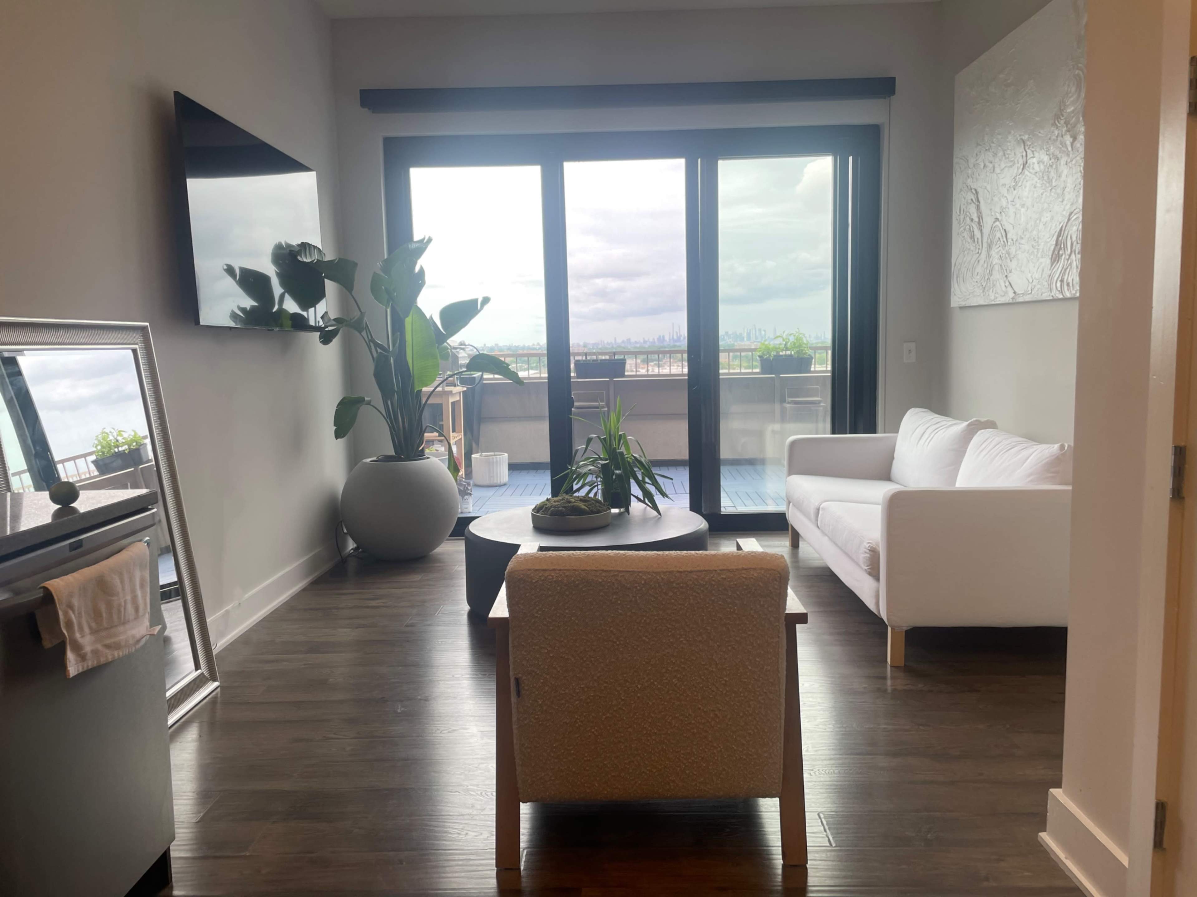A modern living room features a white sofa, a round coffee table, and a large window with a city view.