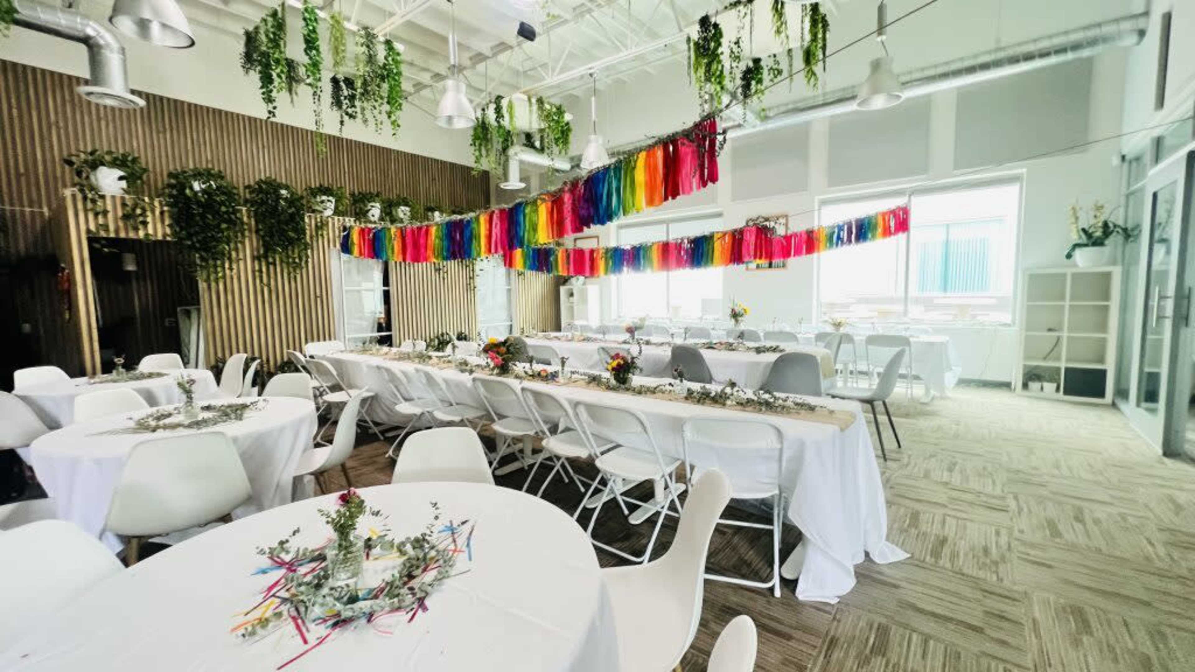 The image shows a bright, modern event space decorated with colorful streamers and tables set for a gathering.
