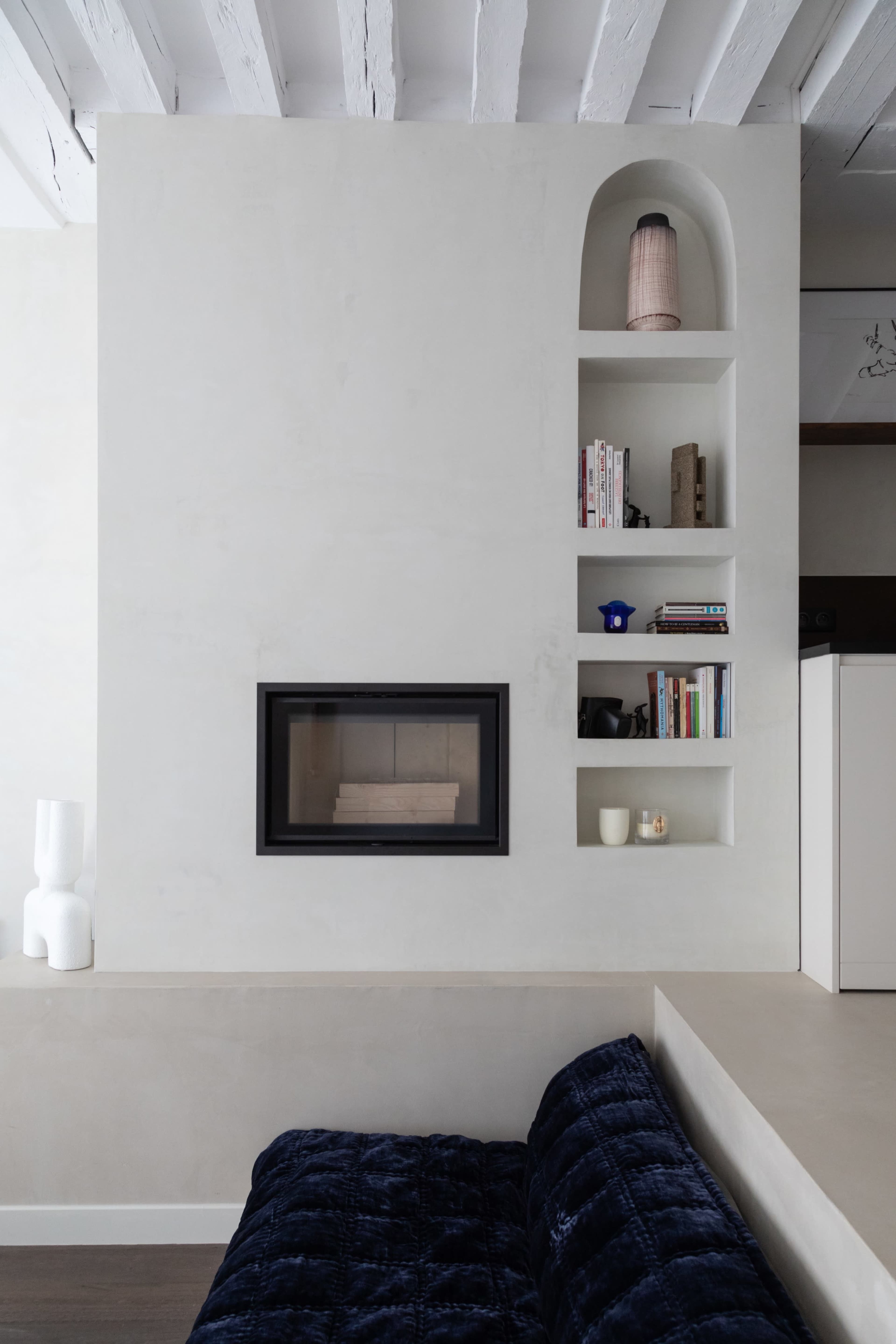 A modern living space featuring a built-in fireplace surrounded by shelves with books and decorative items, alongside a dark blue sofa.