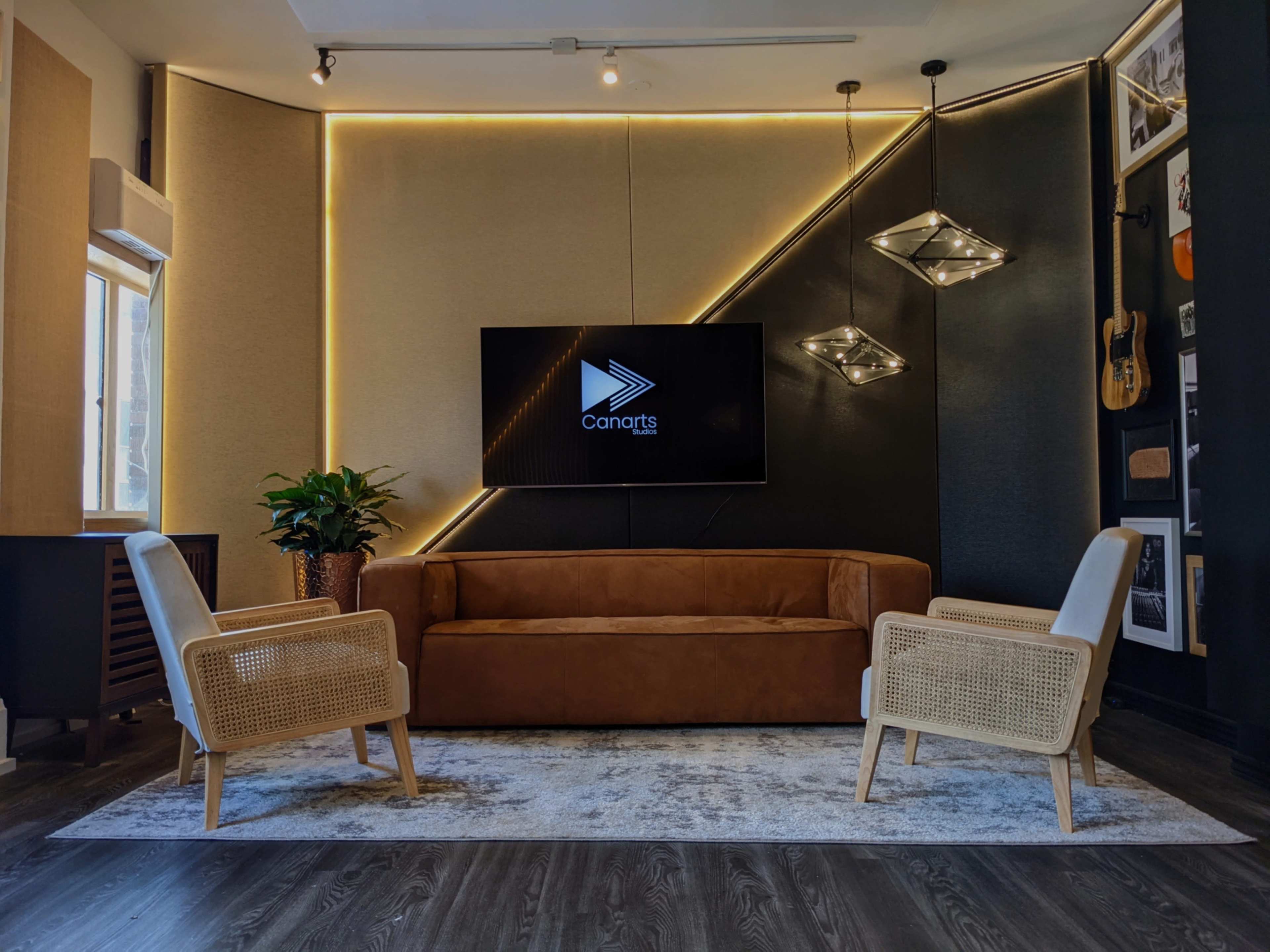 A modern sitting area with a brown sofa, two light-colored chairs, a large television, and decorative lighting elements.