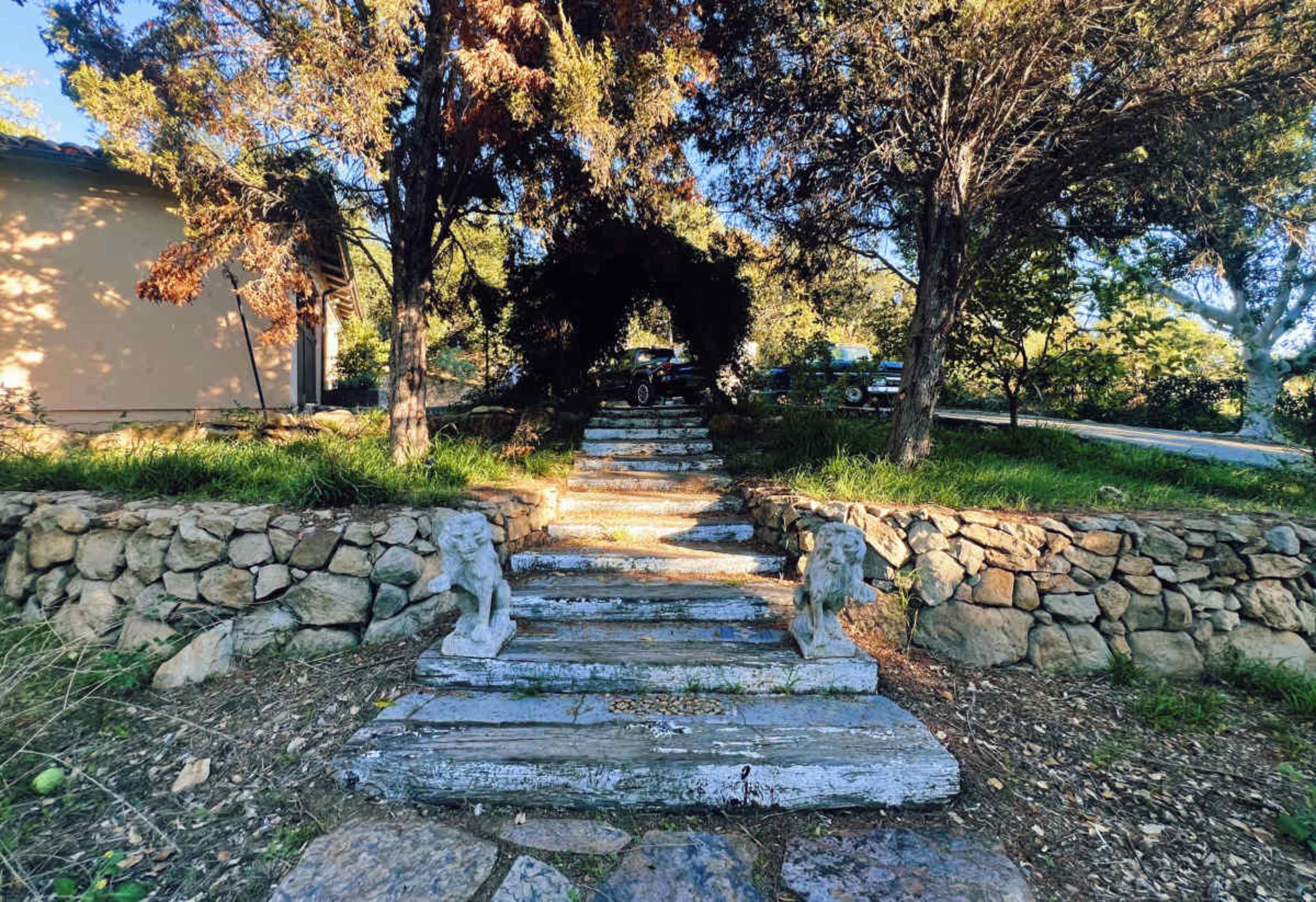 A stone pathway leads up through trees to a house, flanked by two stone lion sculptures.