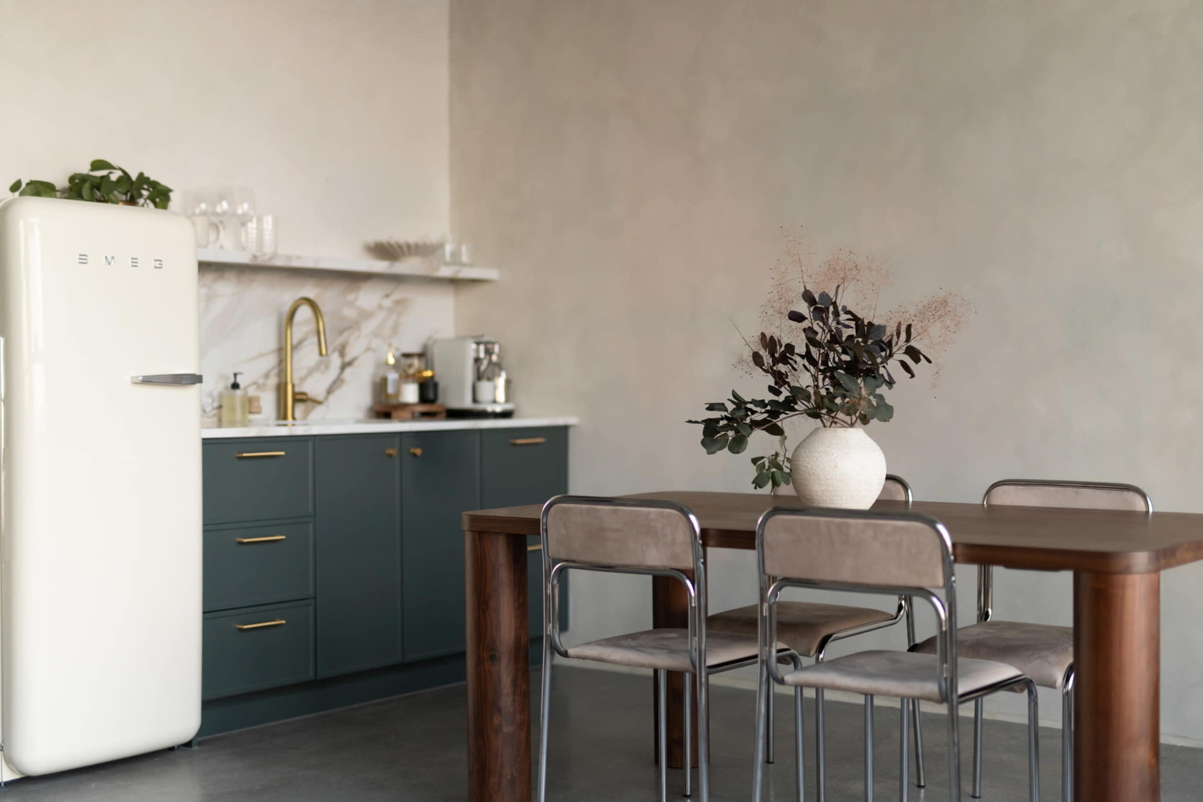 The image features a modern kitchen with a retro-style refrigerator, a marble countertop, and a dining table surrounded by four chairs.