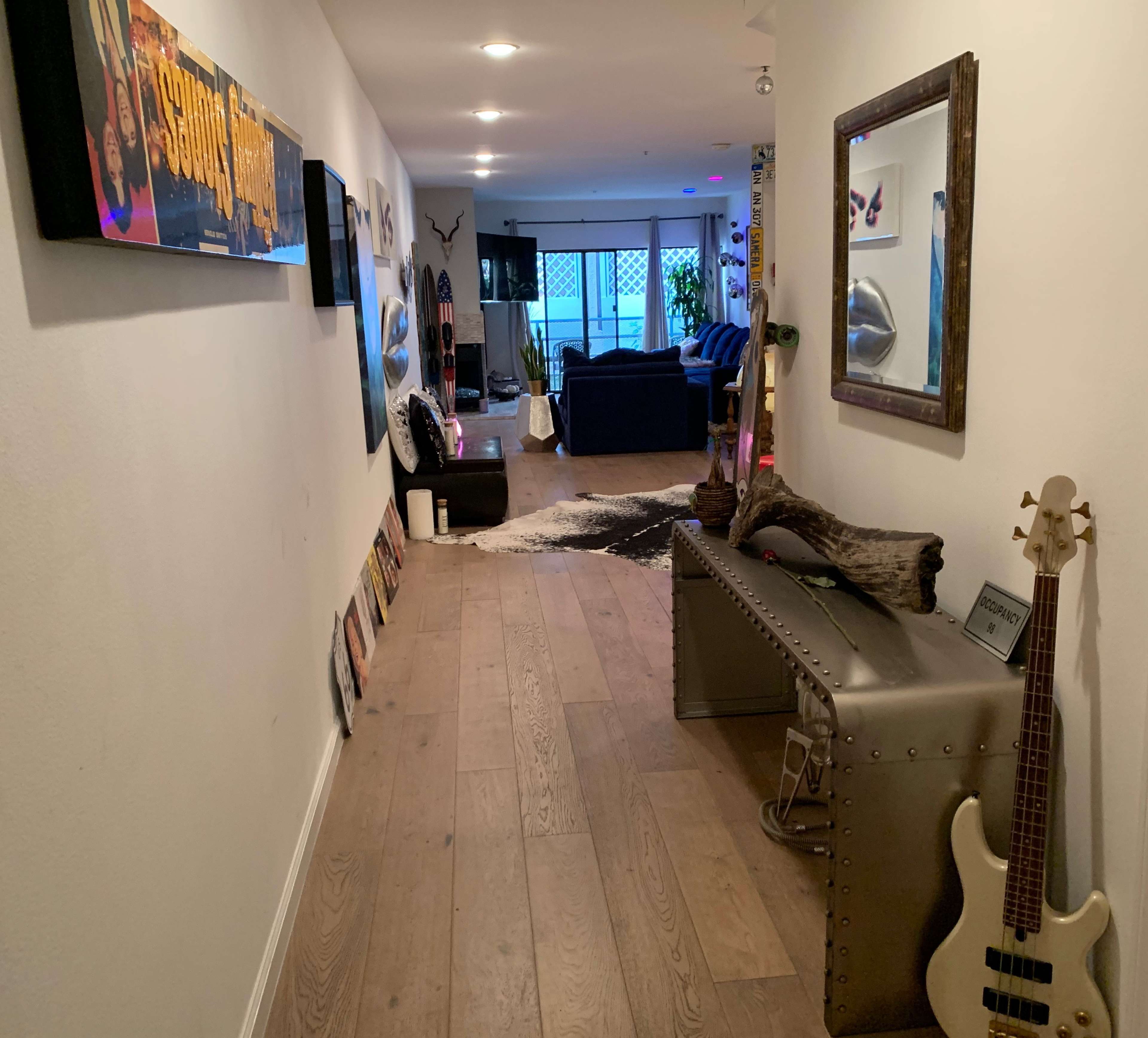 A hallway with light wooden flooring leads to a cozy living area, featuring a couch, wall decorations, and a music-themed display.