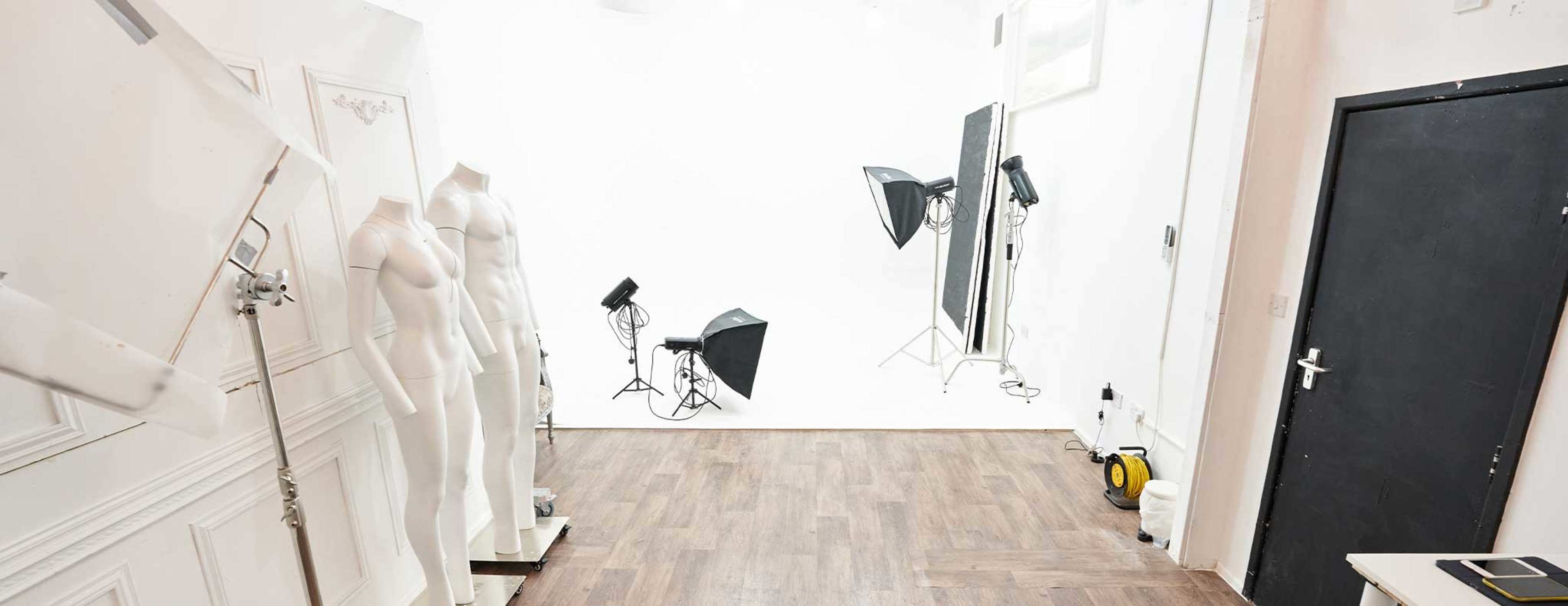A photography studio with blank white walls, floor mannequins, and multiple lighting setups.