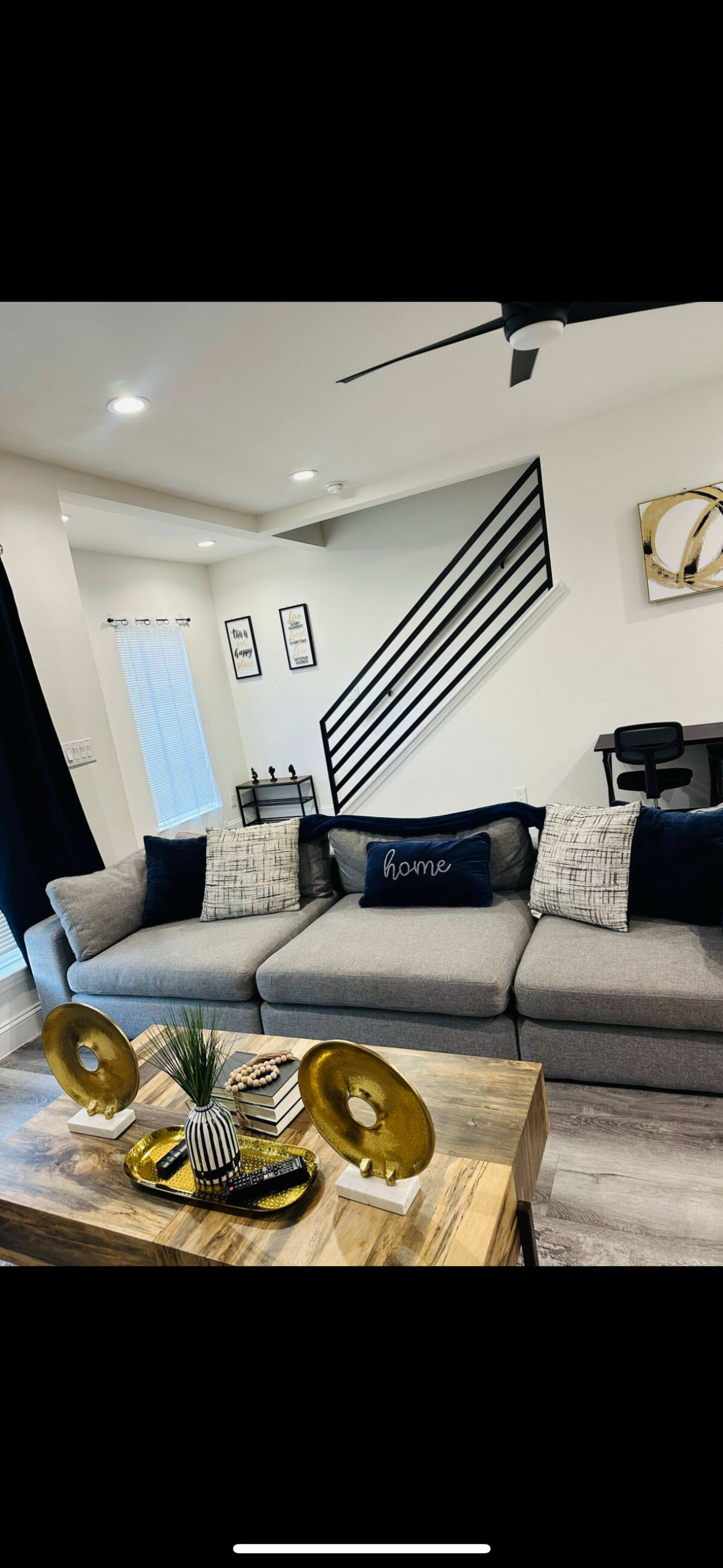 A modern living room with a gray sectional sofa, a wooden coffee table adorned with decorative items, and a staircase in the background.