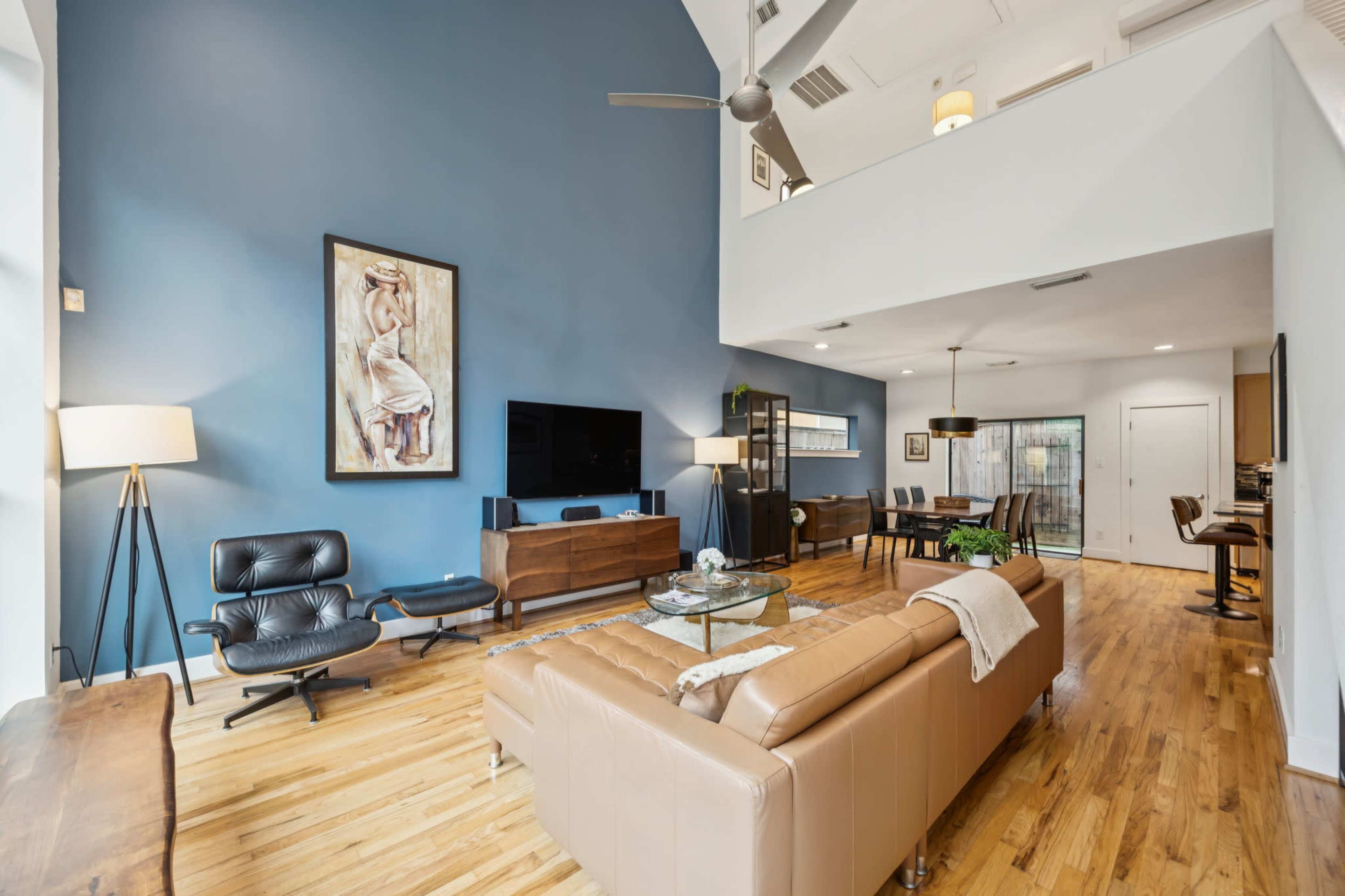 The living area features a blue accent wall, a tan leather sofa, a wooden coffee table, and large windows allowing natural light to fill the space.