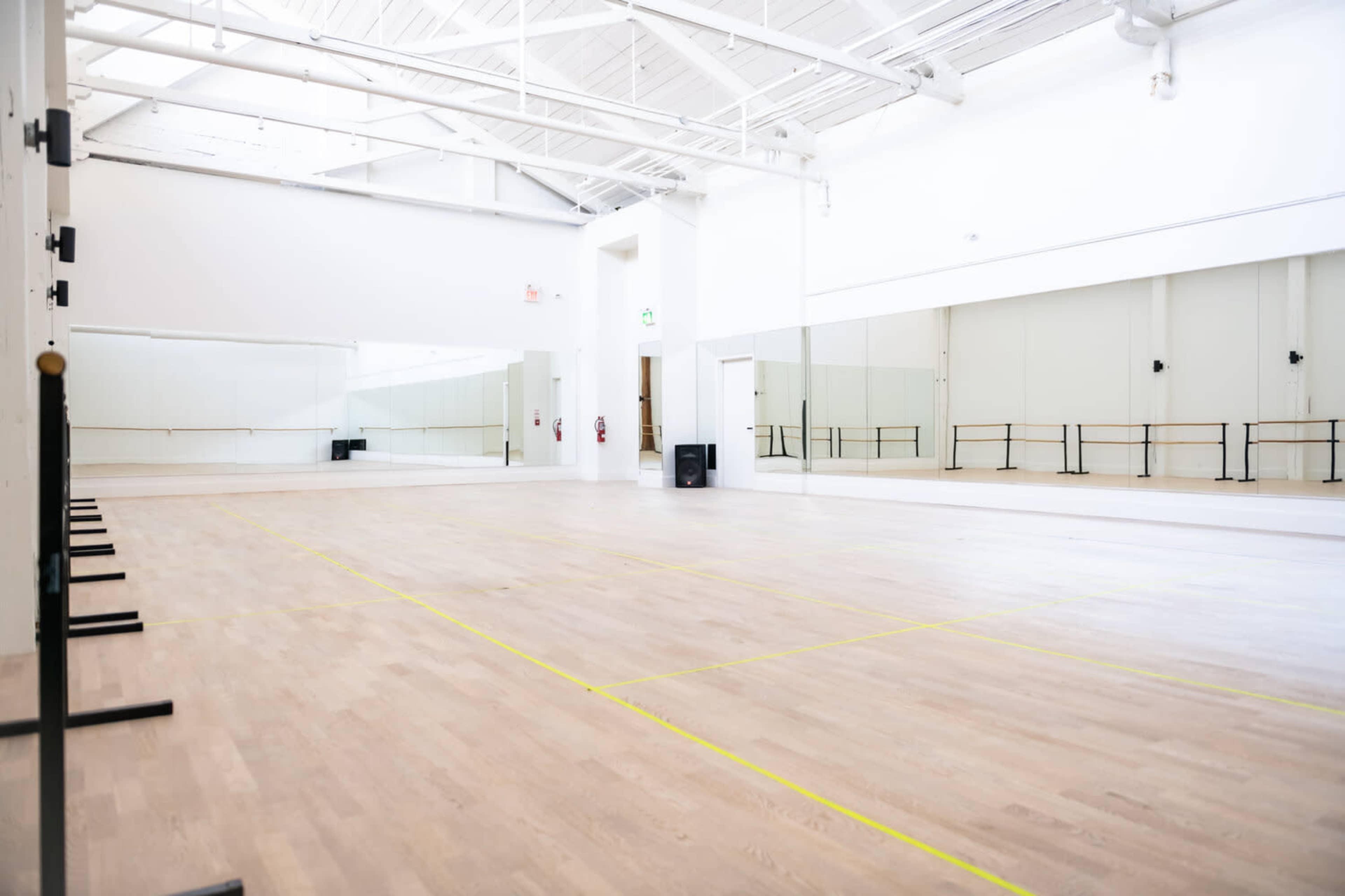 An empty dance studio with wooden flooring, large mirrors on one wall, and ballet barres along the other.