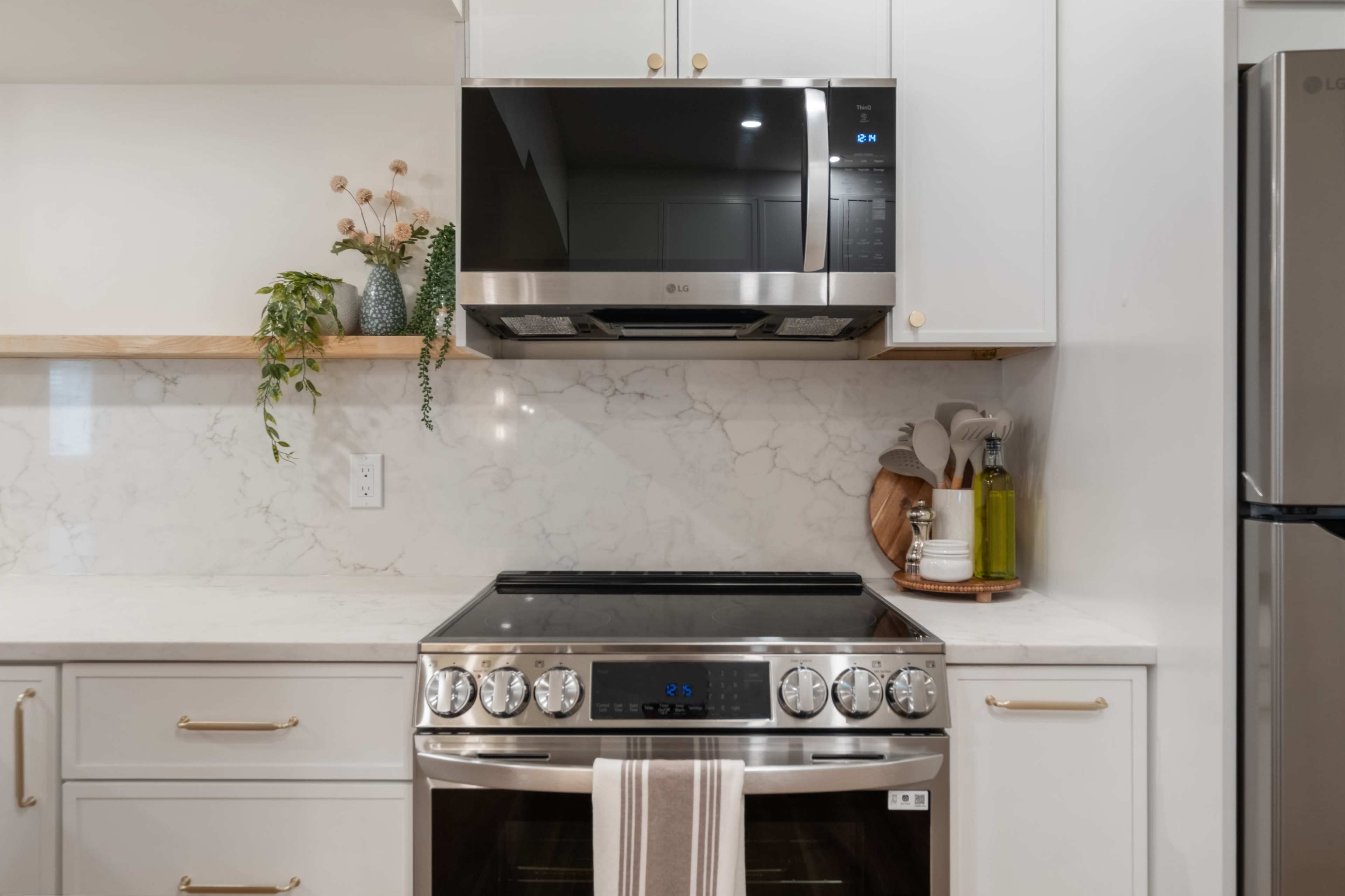 The image shows a modern kitchen with a stainless steel oven and microwave, complemented by white cabinetry and a marble backsplash.