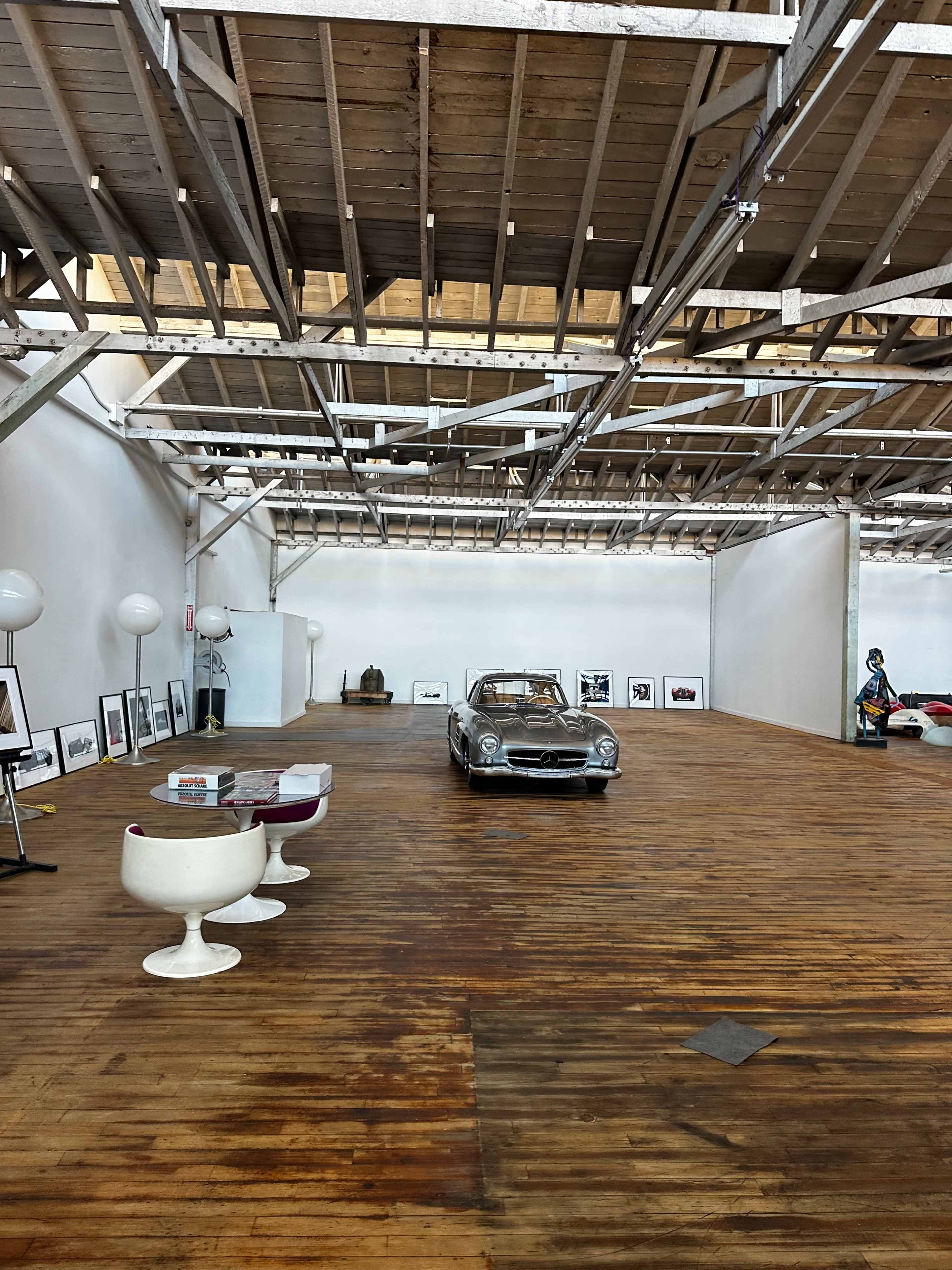 A vintage car is displayed in a spacious gallery with wooden flooring and modern furniture.