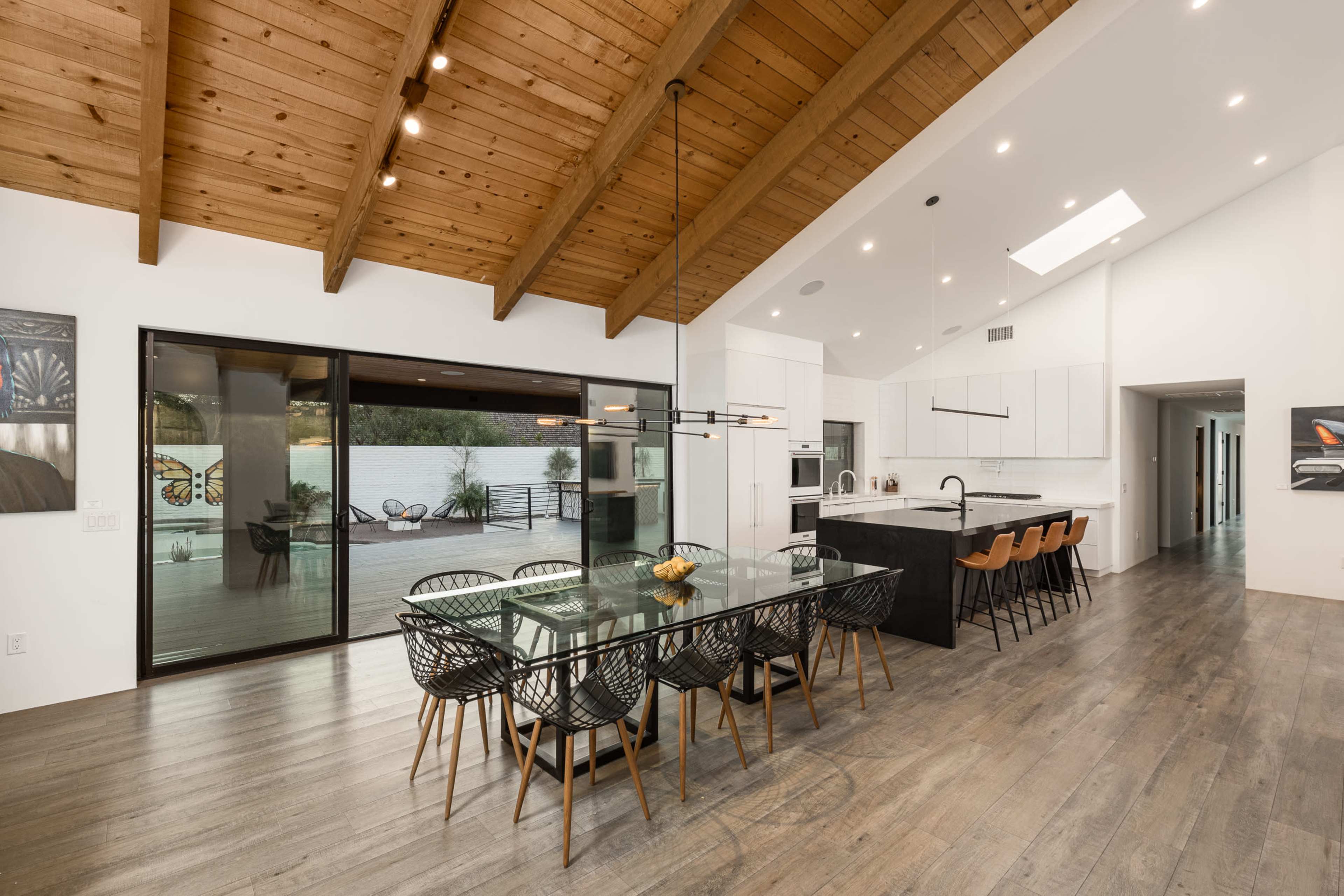 A modern dining area features a large glass table surrounded by black woven chairs, with a view of an outdoor space through large sliding doors.