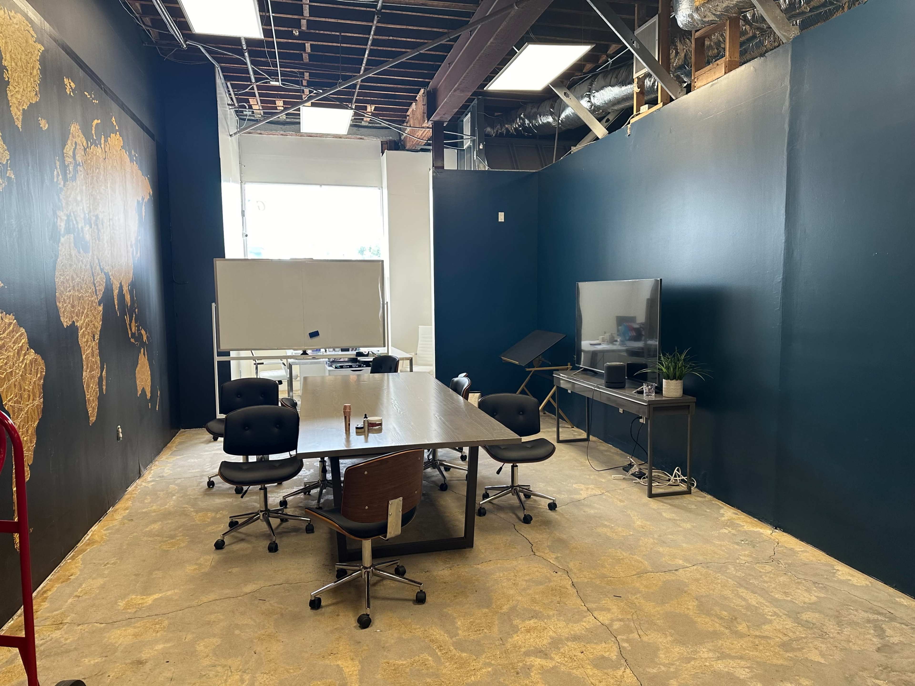 A modern conference room with a large table, several office chairs, a whiteboard, a television, and a map of the world on the wall.
