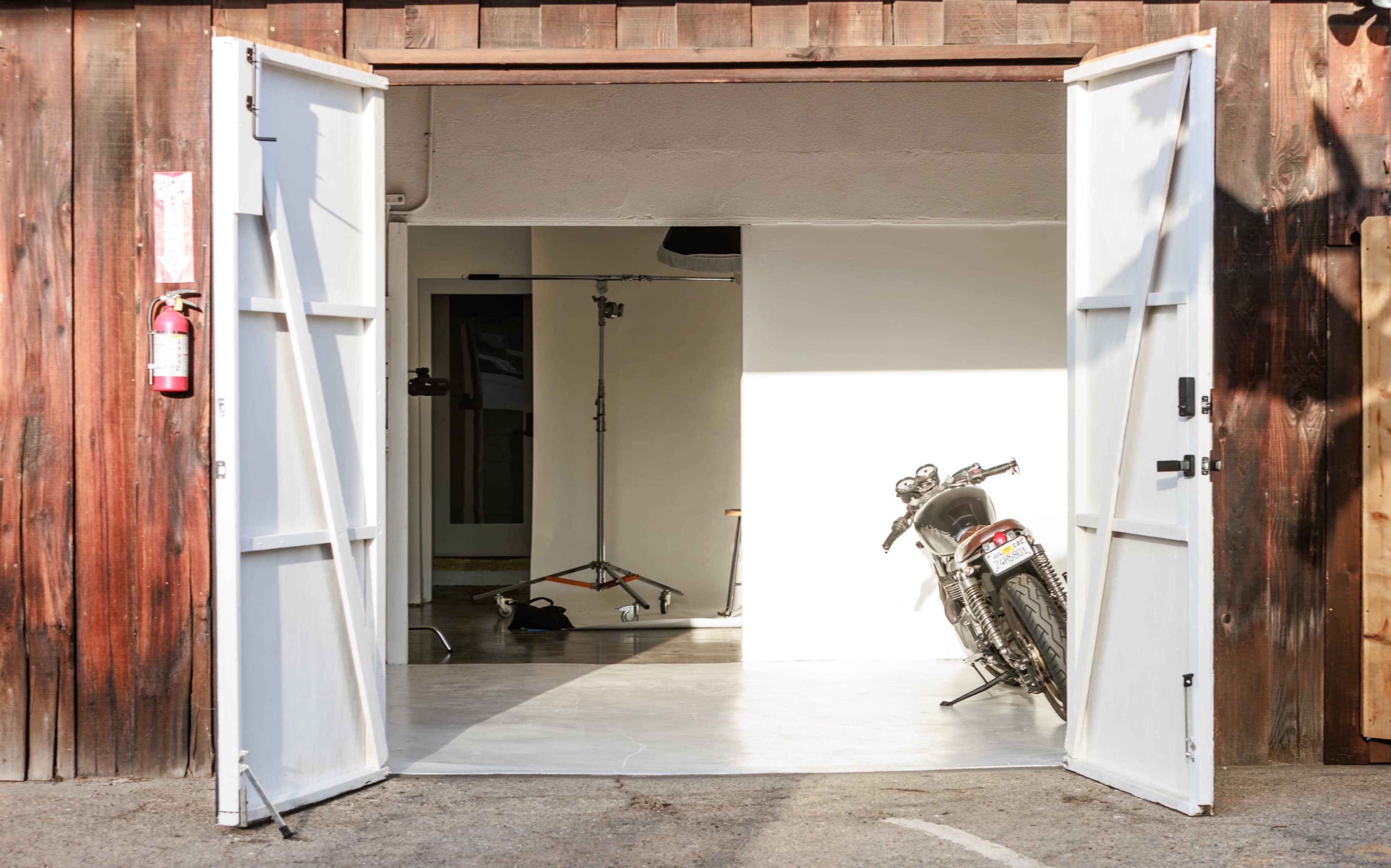 A motorcycle is parked at an angle inside a brightly lit studio with open double doors.