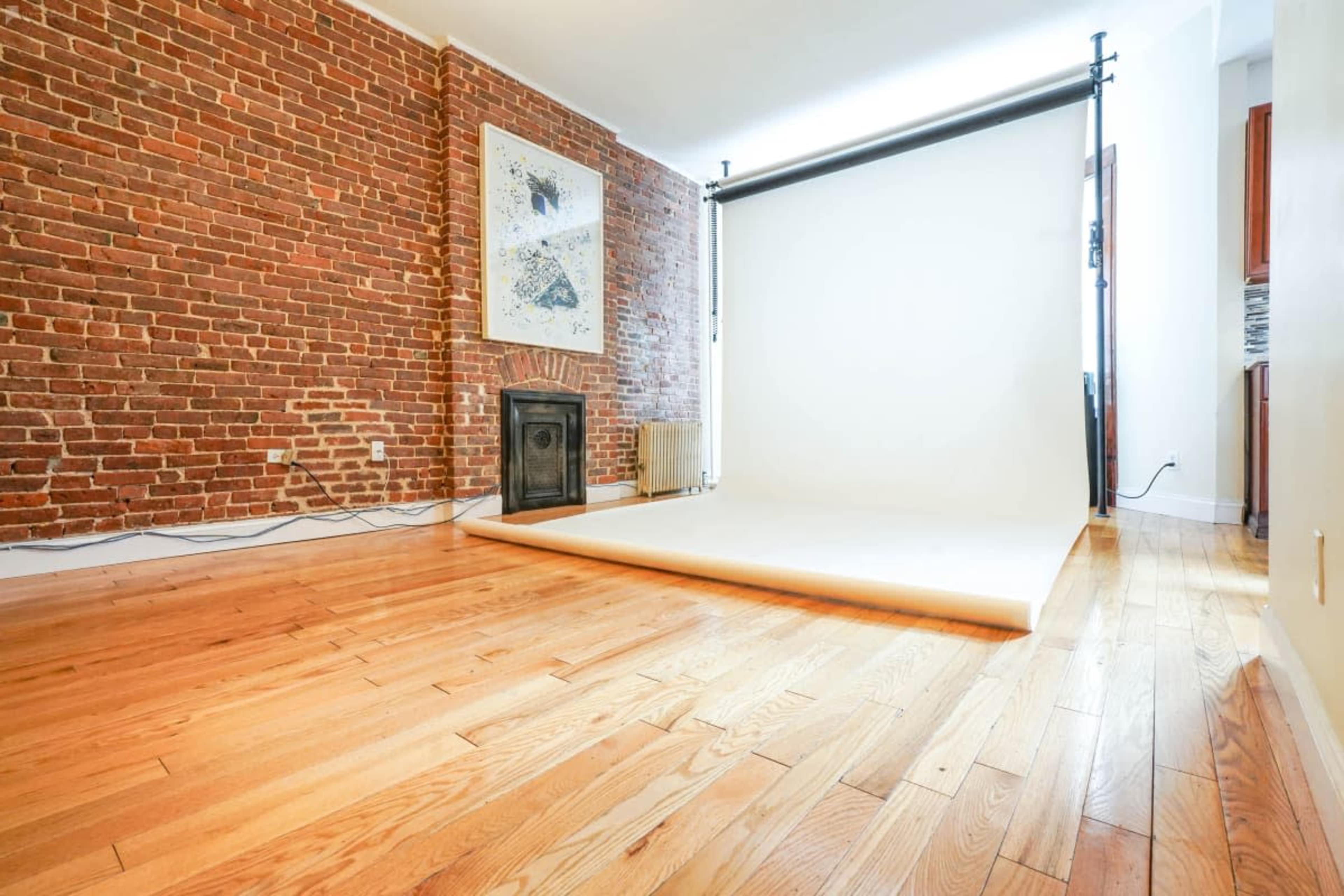 A spacious room with exposed brick walls, a white backdrop set for photography, and hardwood flooring.