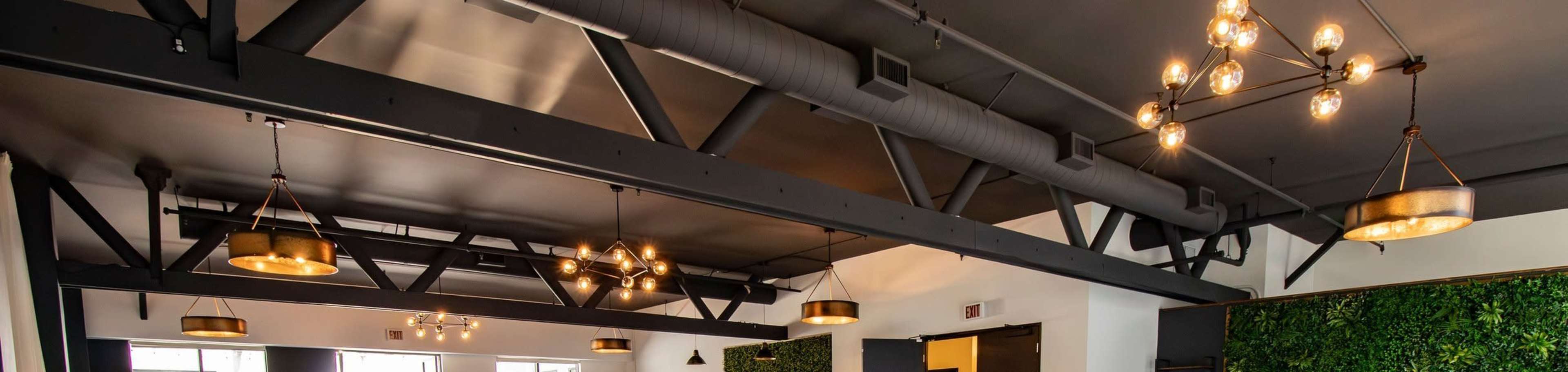 An interior space featuring industrial-style lighting fixtures, exposed beams, and green wall accents.