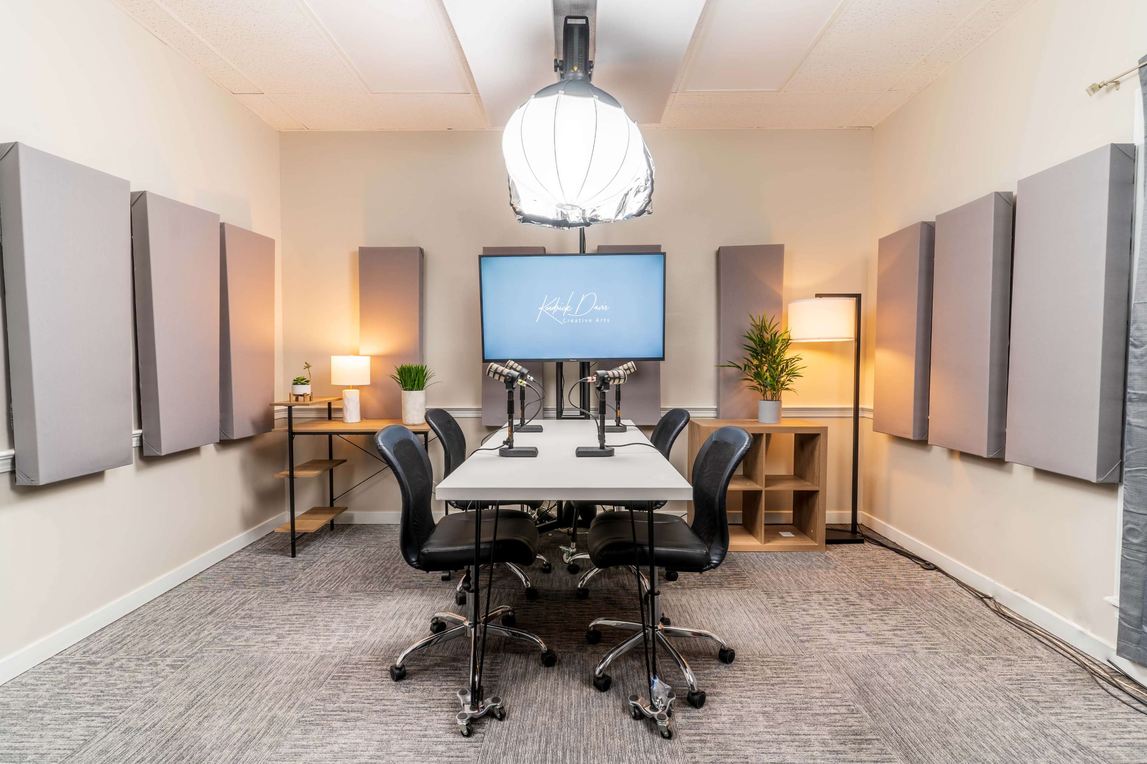 A modern conference room equipped with a central table, four black chairs, a large screen, and soundproof wall panels.