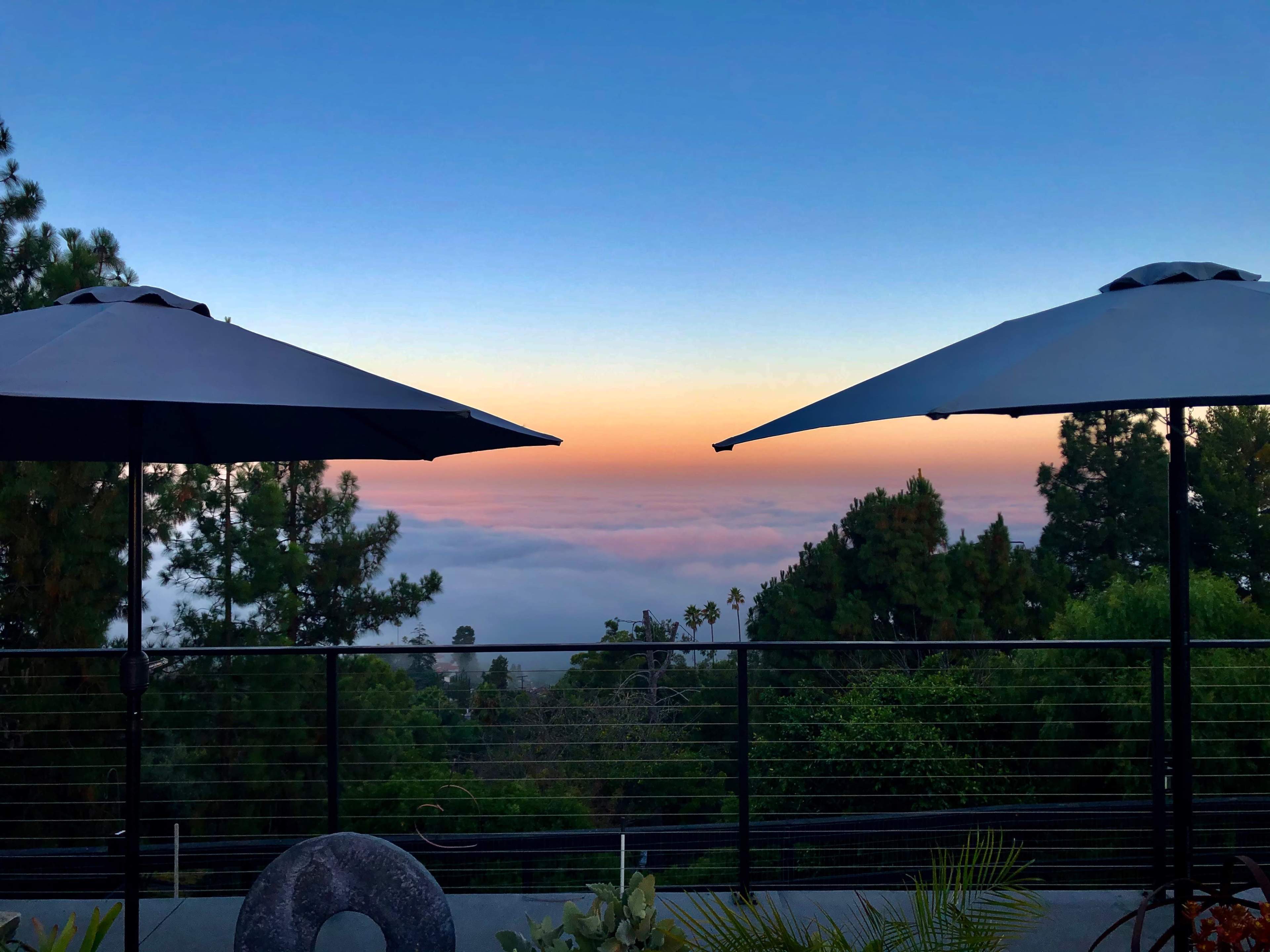 Two black umbrellas positioned on a balcony overlooking a sea of clouds and a colorful sunrise.