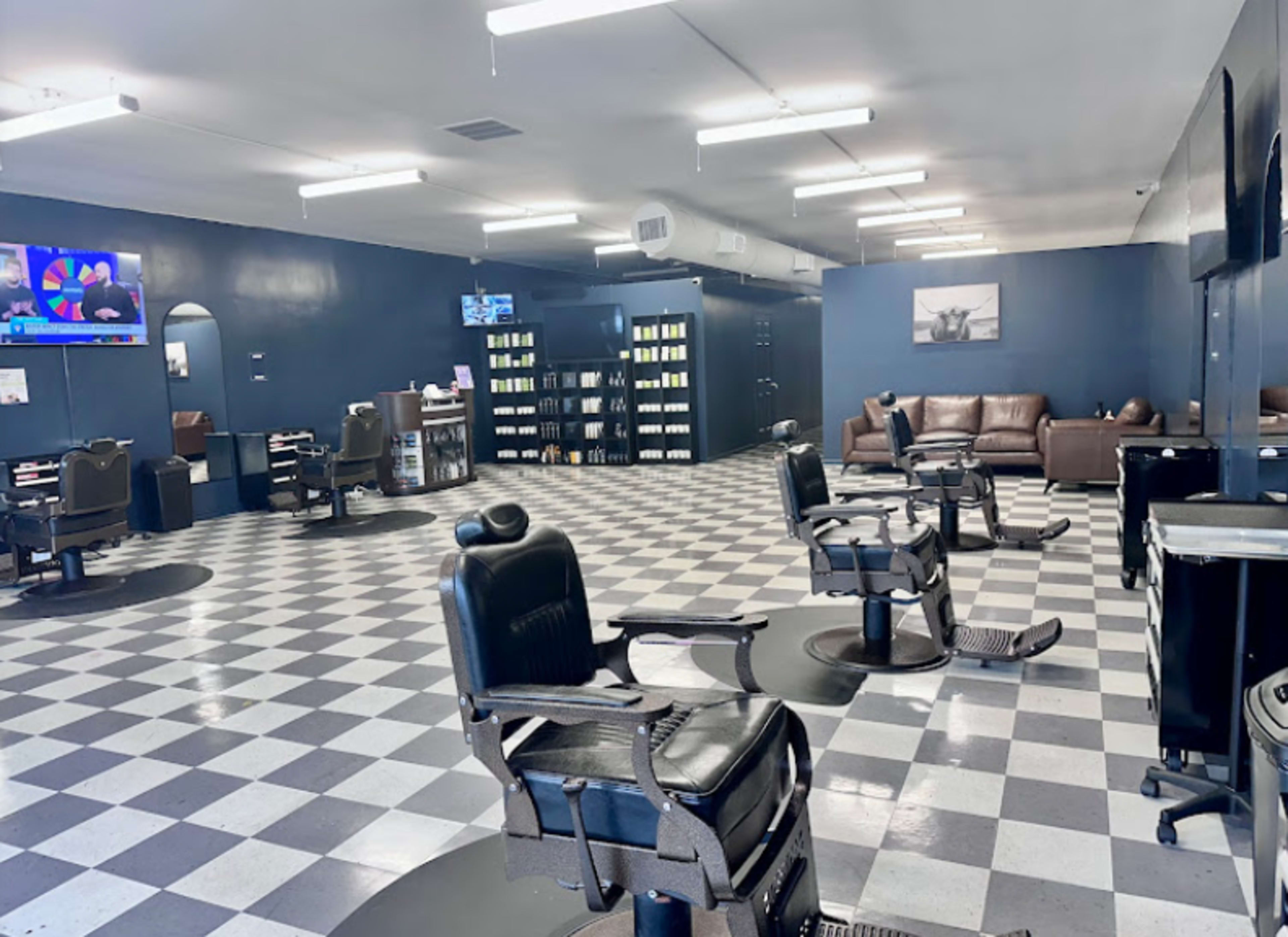 The image shows a spacious barbershop with black and white checkered flooring, several barber chairs, and a waiting area with a leather couch.
