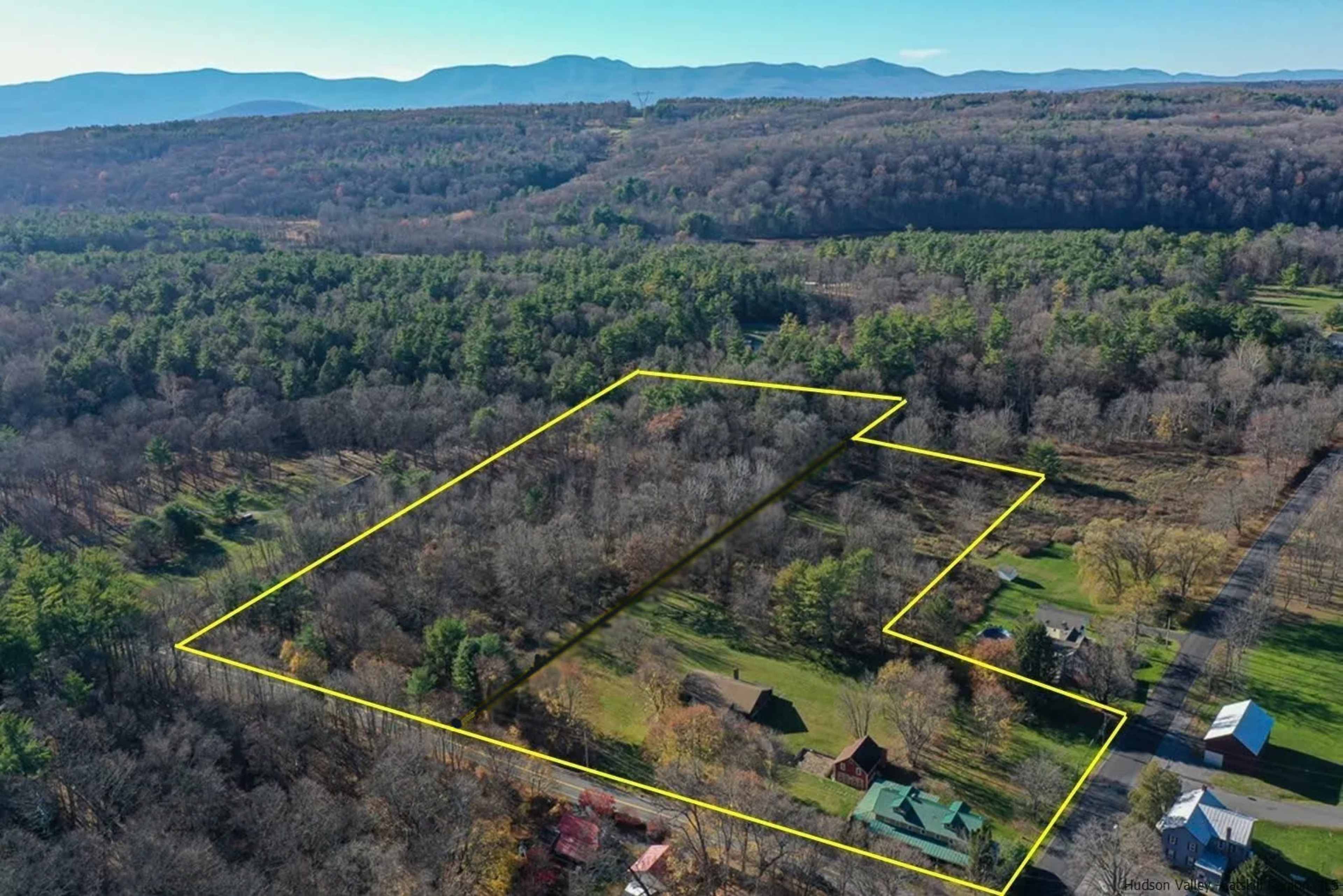 An aerial view shows a spacious, wooded property outlined in yellow, set against a backdrop of mountains and clear sky.