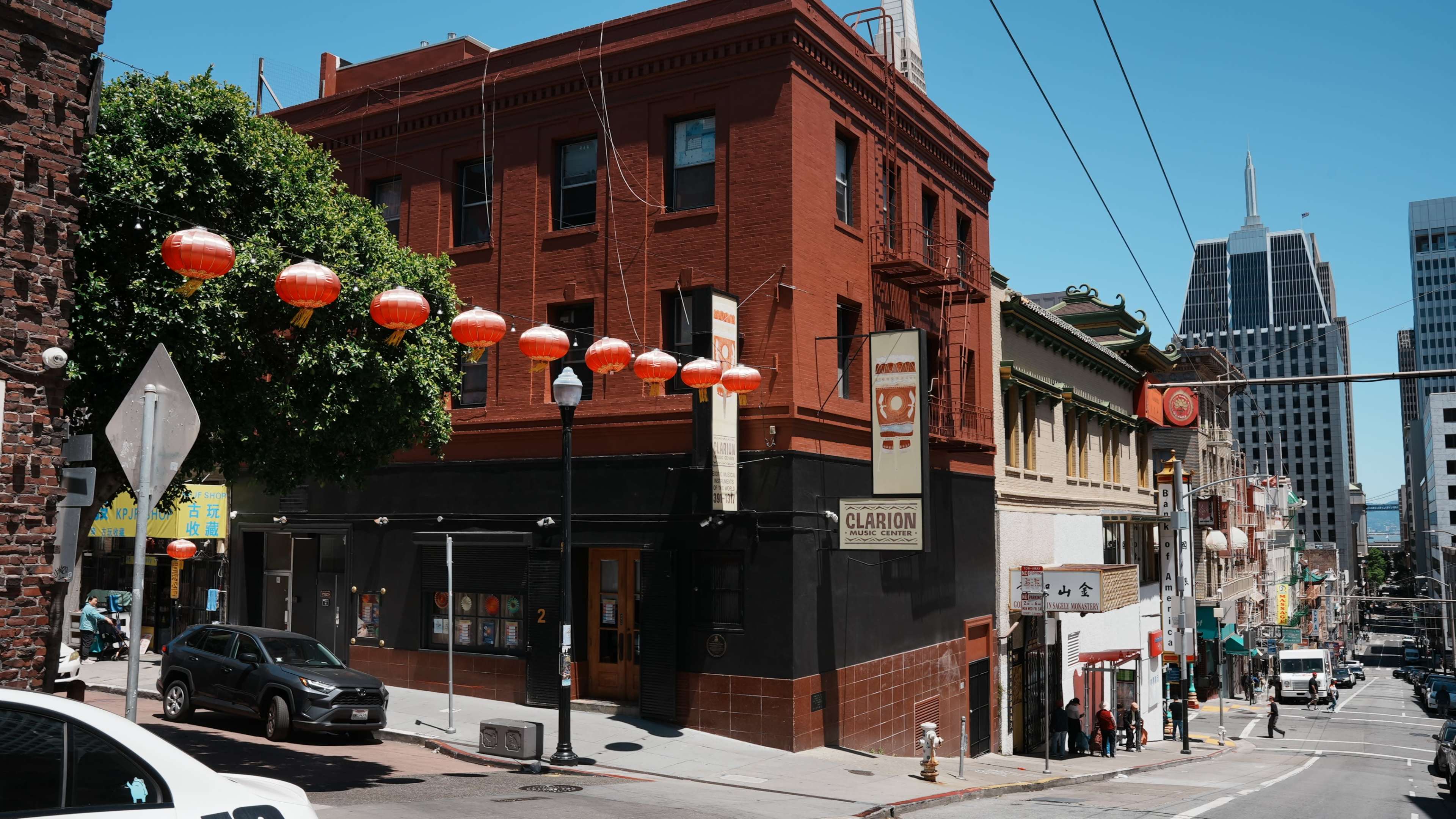The image shows a historic red-brick building at the corner of a bustling street, adorned with lanterns, in a city likely featuring a Chinatown.