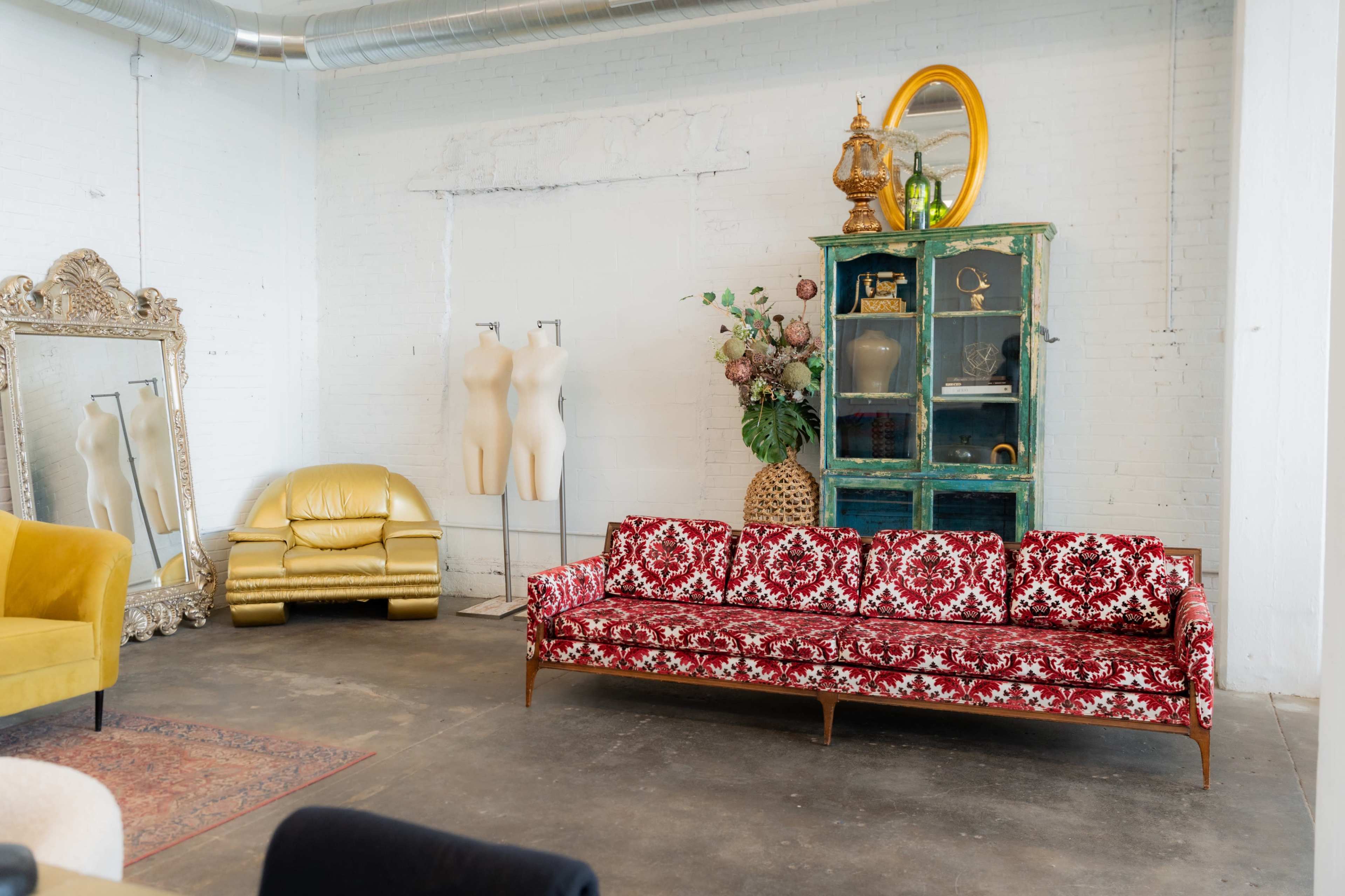 The scene features a red patterned sofa in a minimalist room with a green cabinet, a large mirror, and a yellow chair.