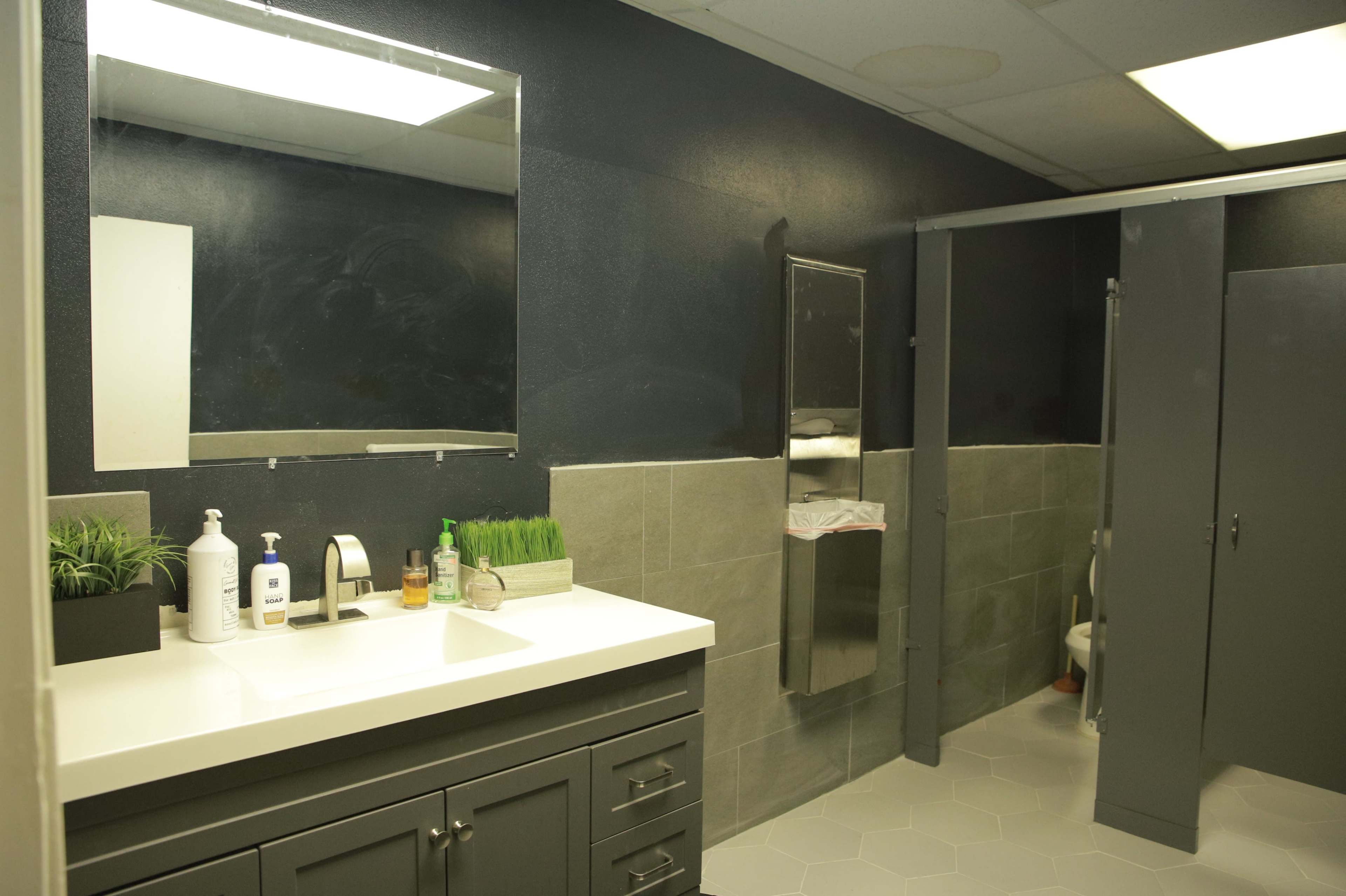 A modern bathroom featuring a dark wall color, a white countertop with toiletries, and a separate shower area.