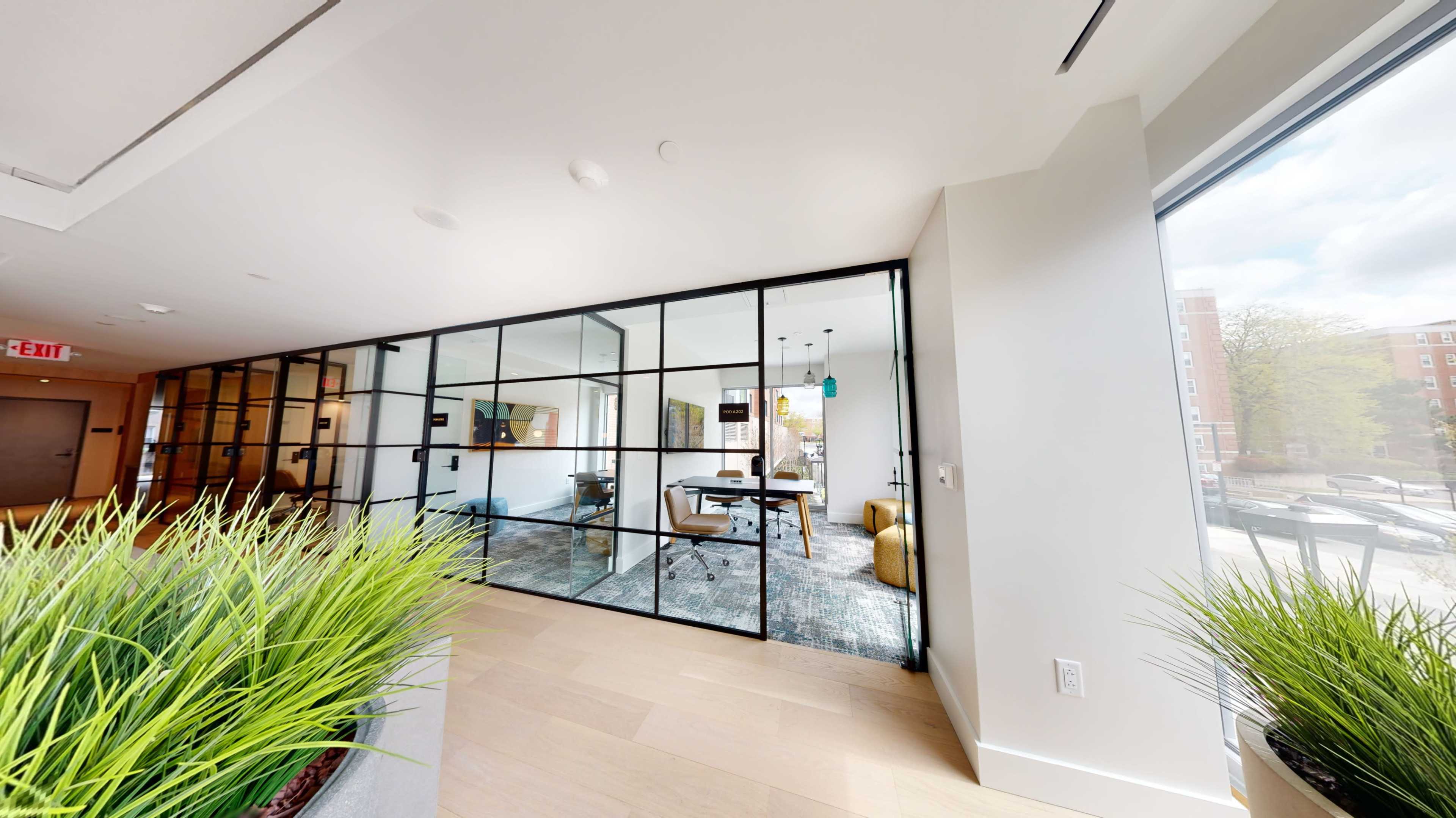The image shows a modern office space with glass walls, a conference table, and views of greenery outside.