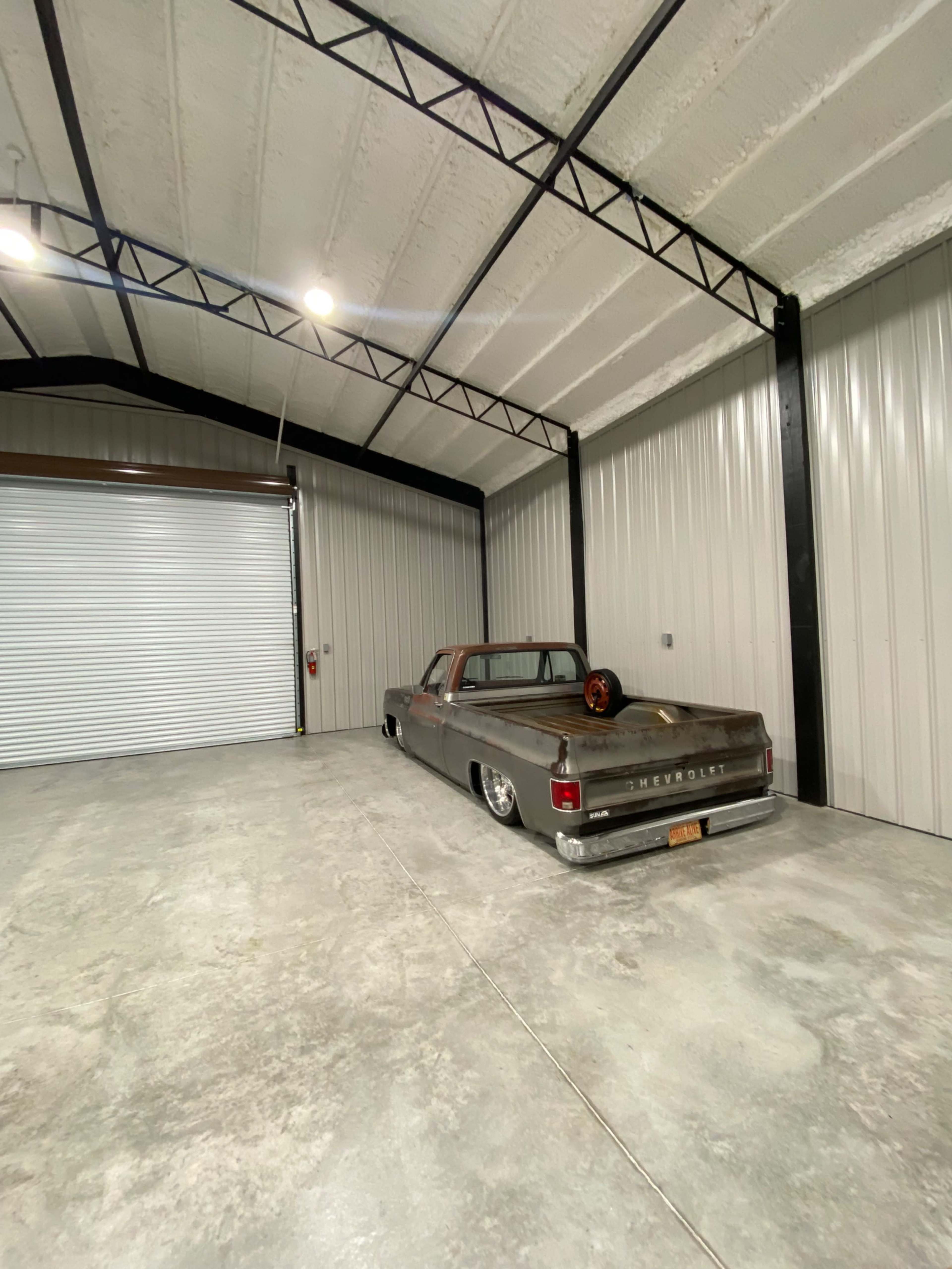 A vintage Chevrolet truck is parked in a spacious garage with metal walls and a roll-up door.