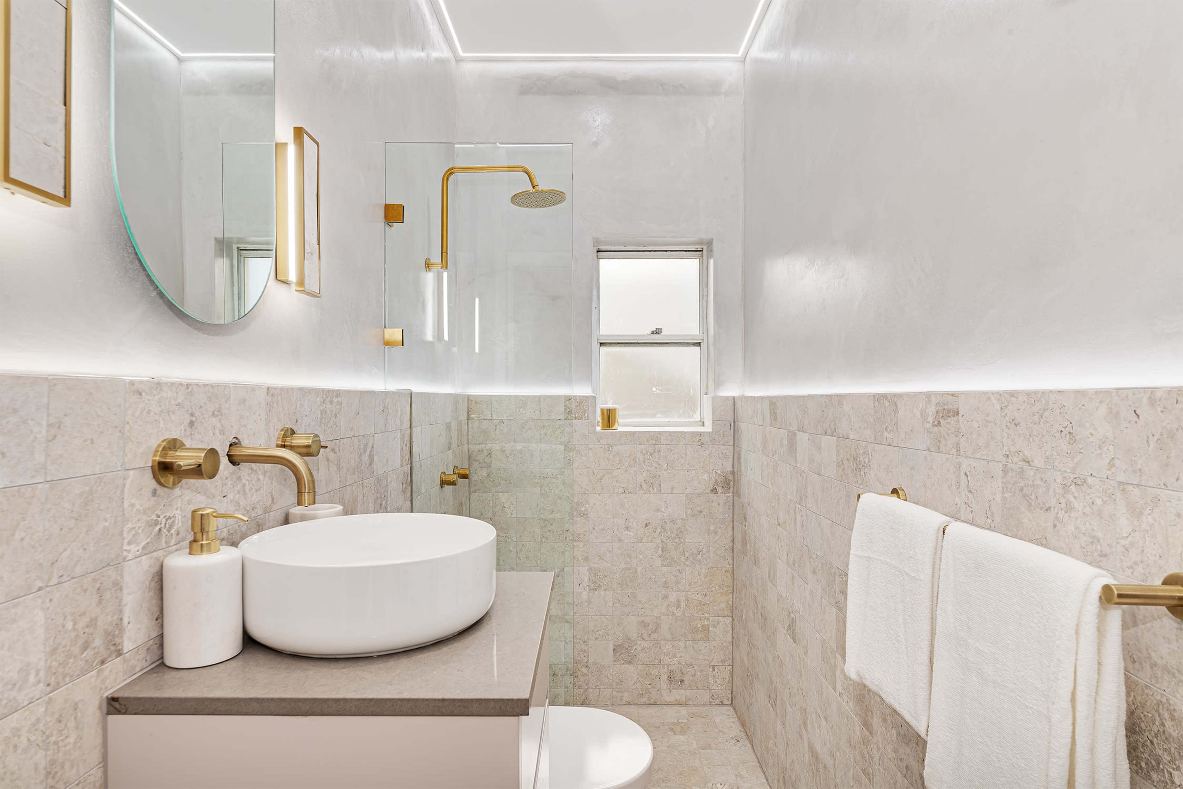 A modern bathroom with a shower, a circular mirror, a circular sink on a countertop, and beige tiled walls.