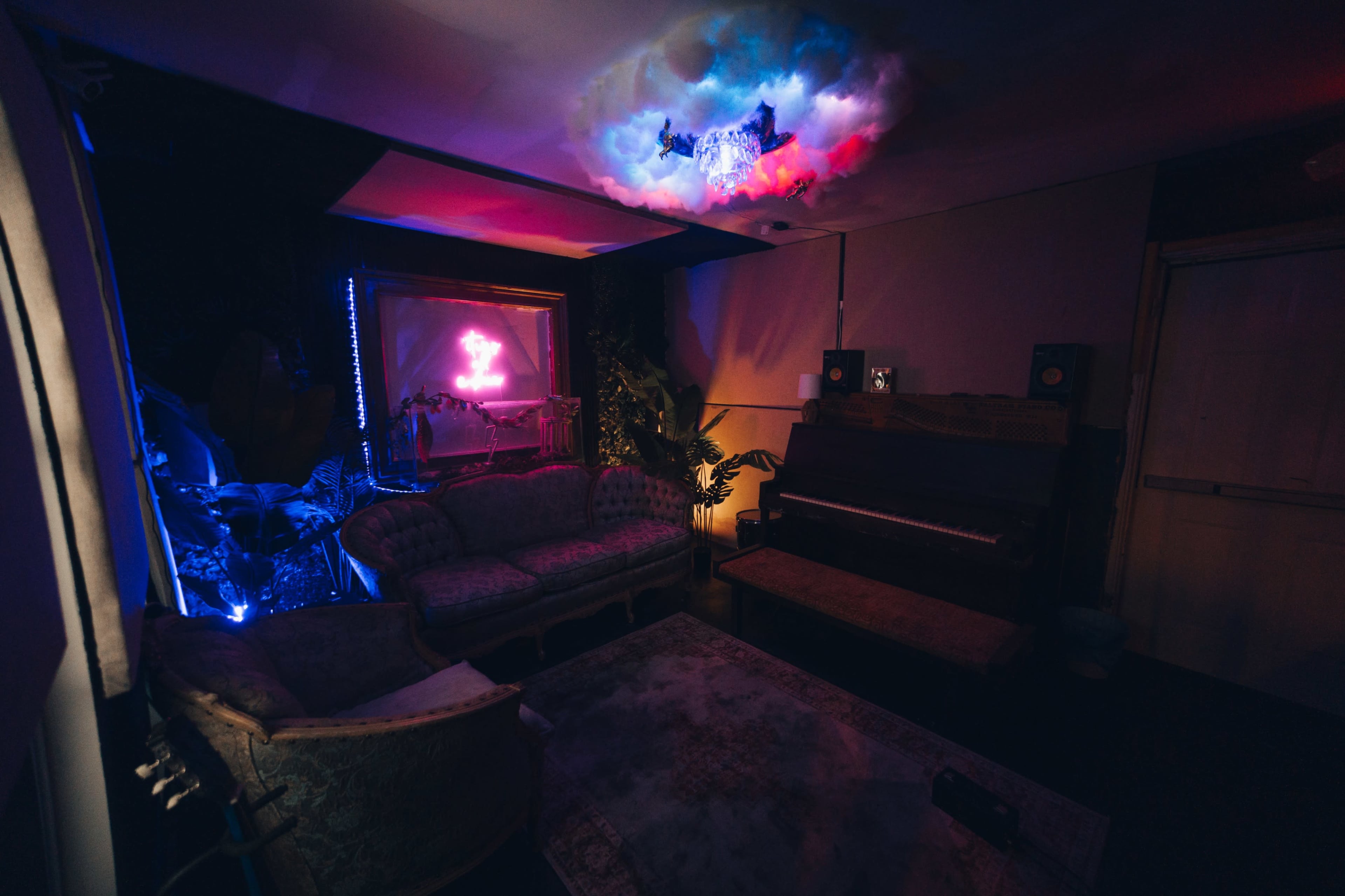 The image shows a dimly lit room with vintage furniture, a piano, and colorful lighting effects from a decorative chandelier.