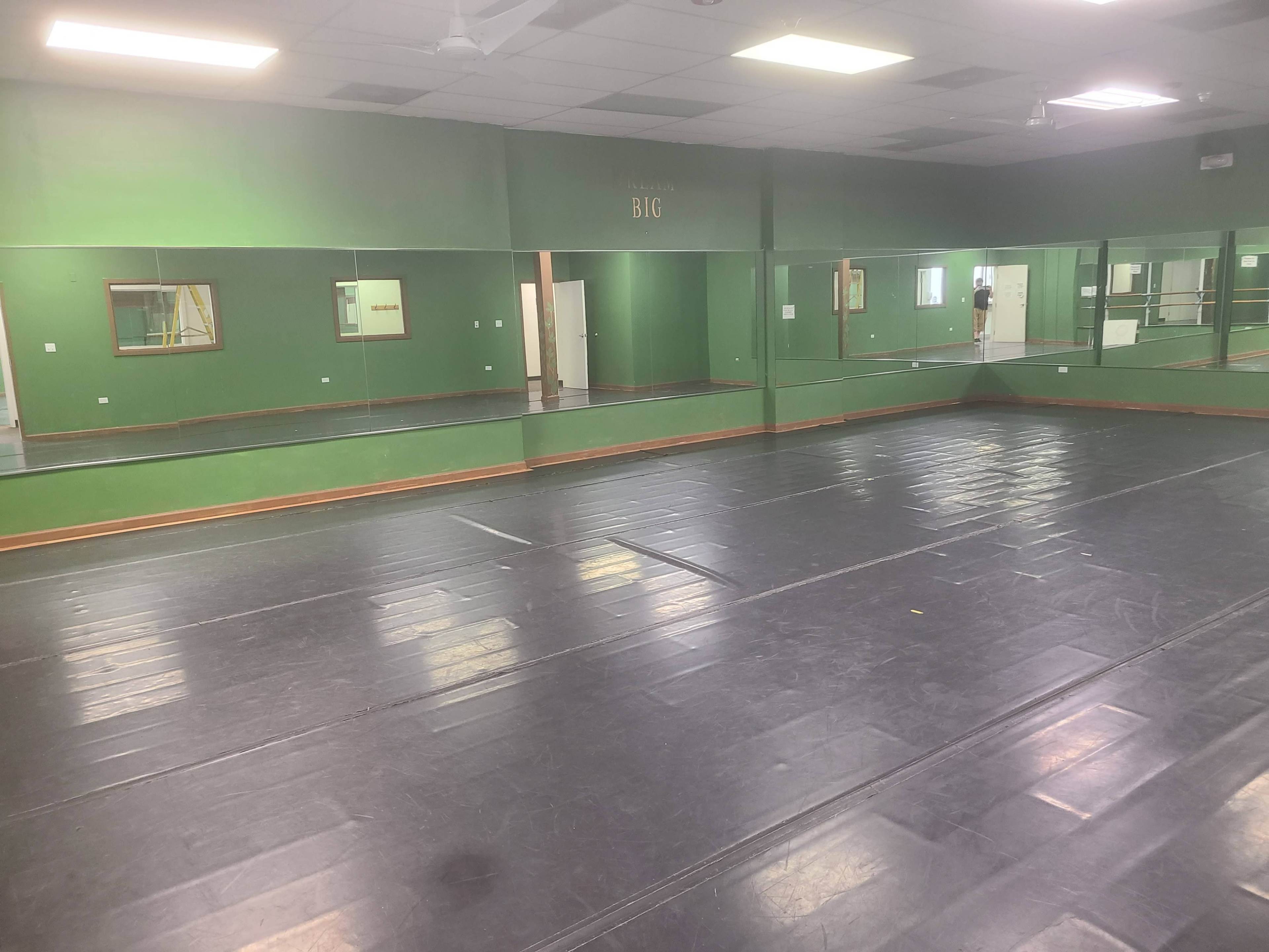 An empty dance studio with green walls, mirrored walls, and a polished black floor.