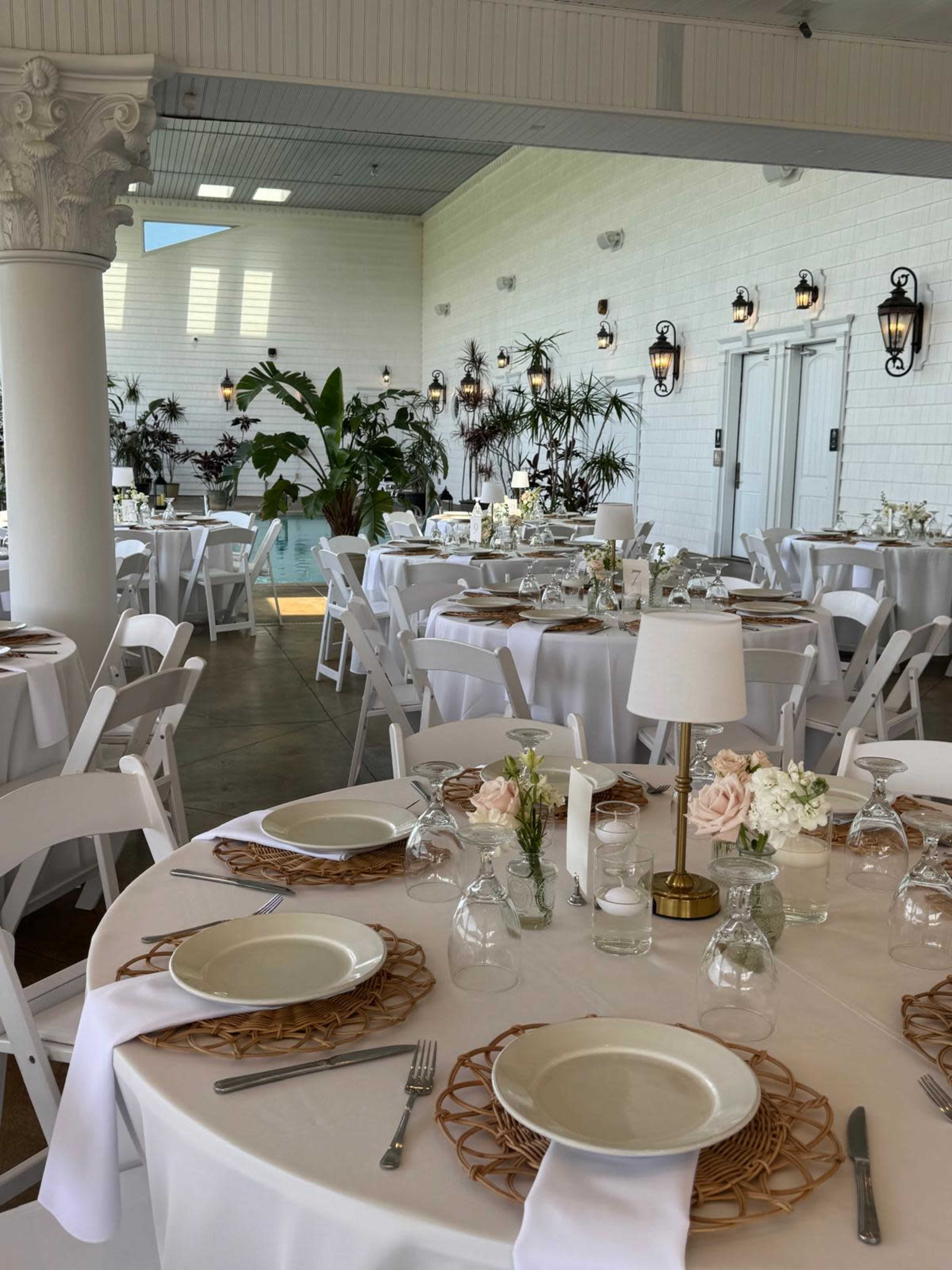 The image shows a banquet hall arranged for a formal event with round tables set with white tablecloths, centerpieces, and dining ware.