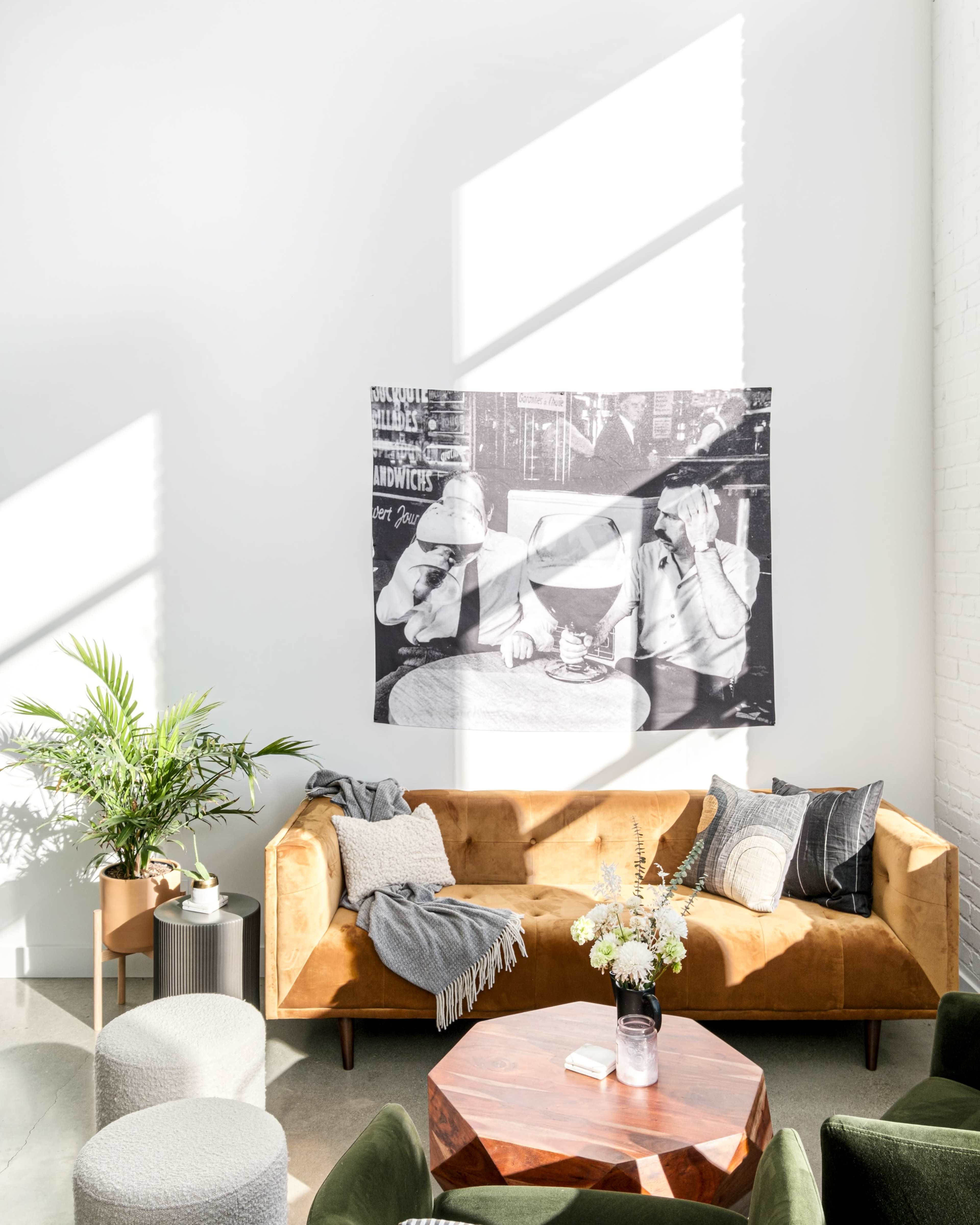 A cozy living room features a brown velvet sofa, a circular wooden coffee table, and a large black-and-white photograph on the wall.