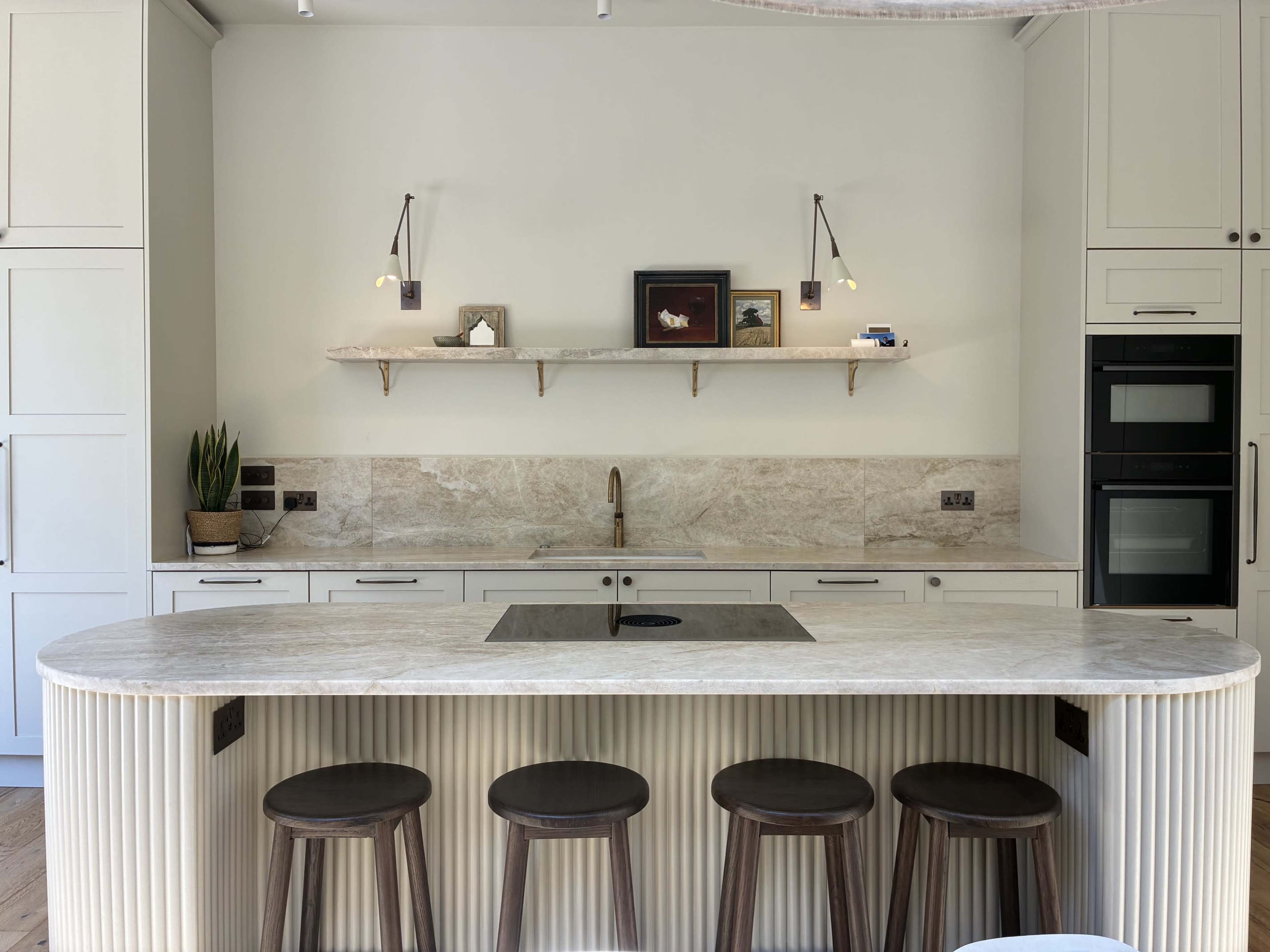 The image shows a modern kitchen featuring a marble countertop with four wooden stools, a minimalist design, and natural wood accents.