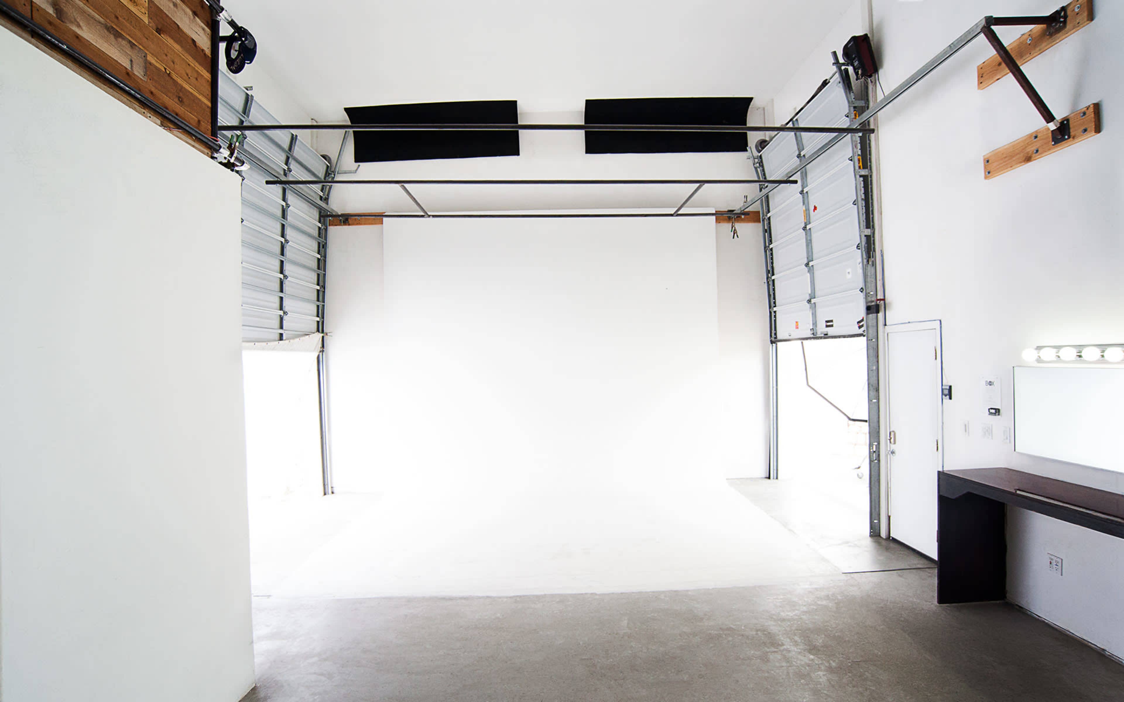 A large, empty studio space with a white backdrop and large garage doors on one side.