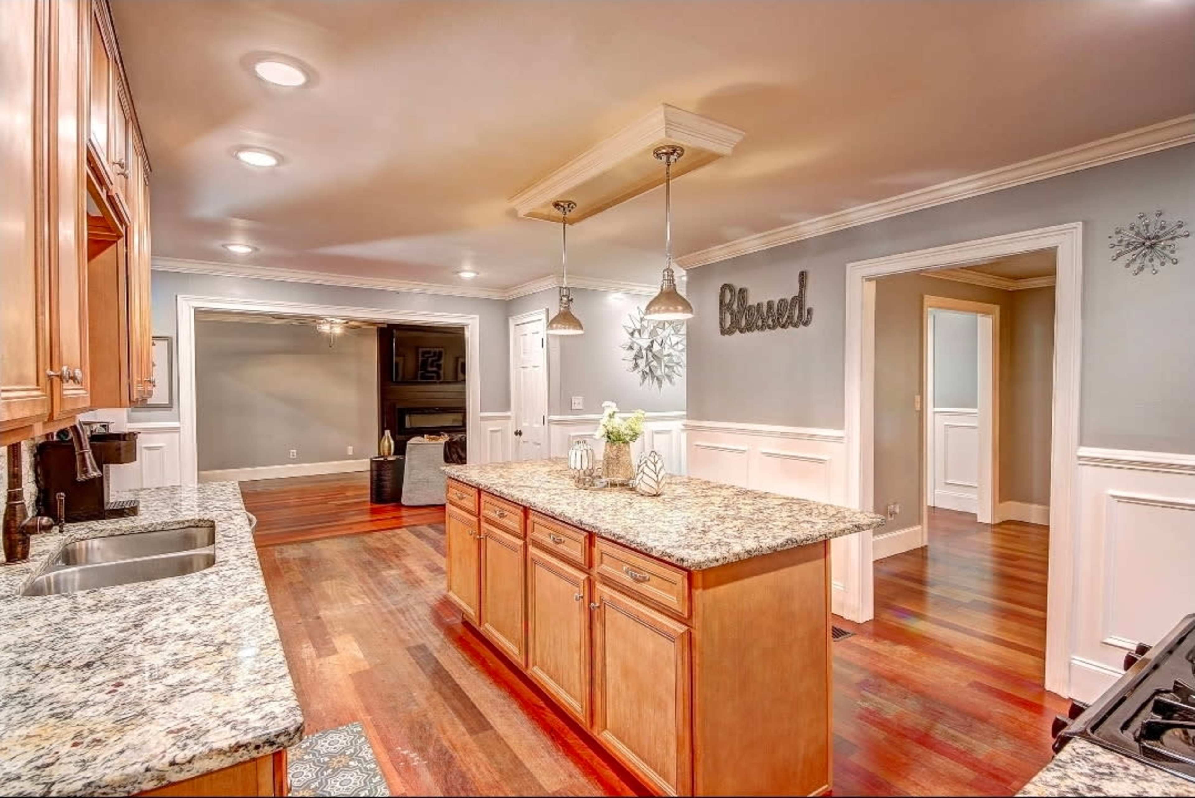 A modern kitchen features wooden cabinets, a central island with granite countertops, and decorative lighting fixtures above.