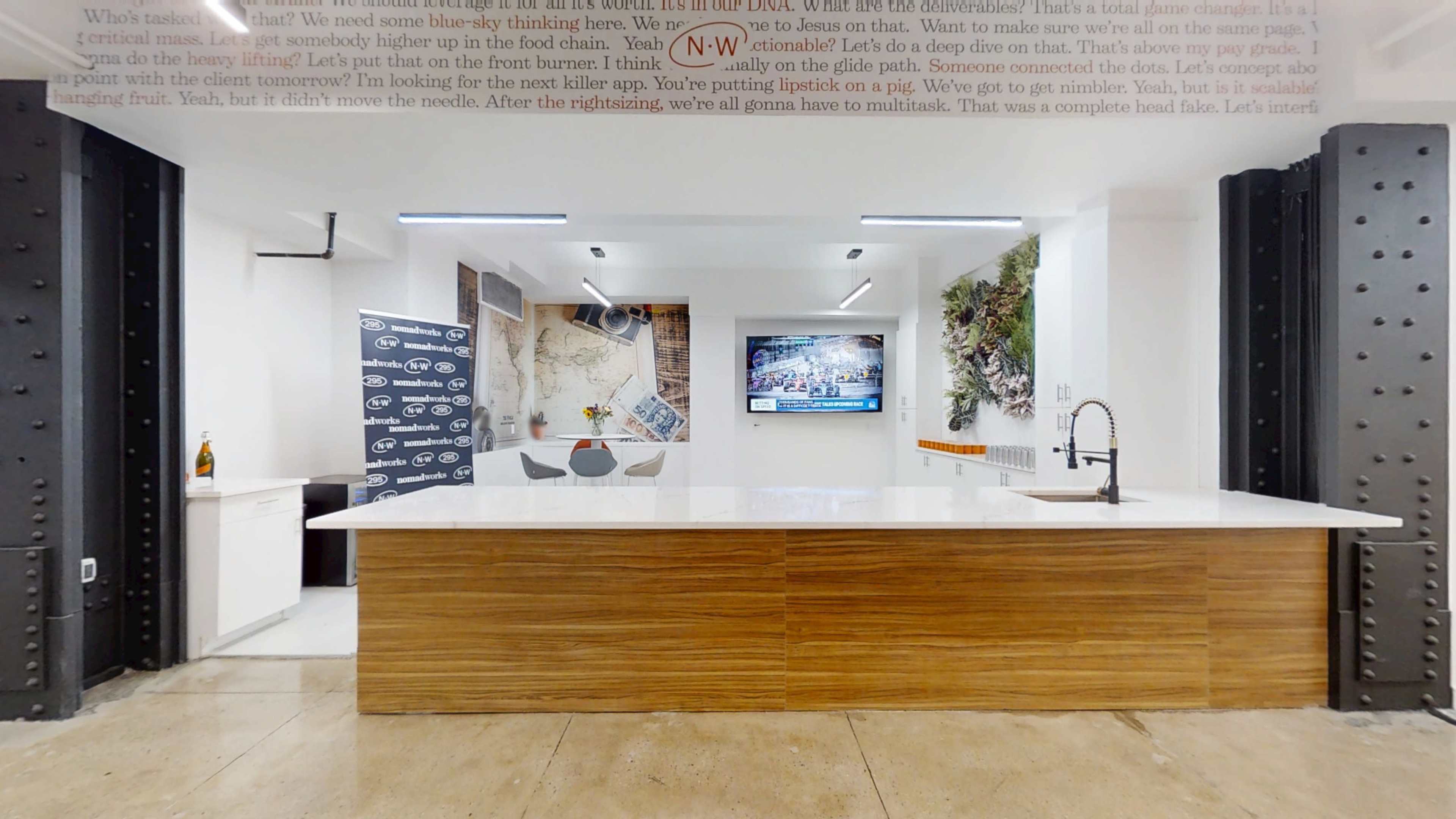 The image shows a modern kitchen space with a large island counter, a sink, and wall decor featuring a map and a television on display.