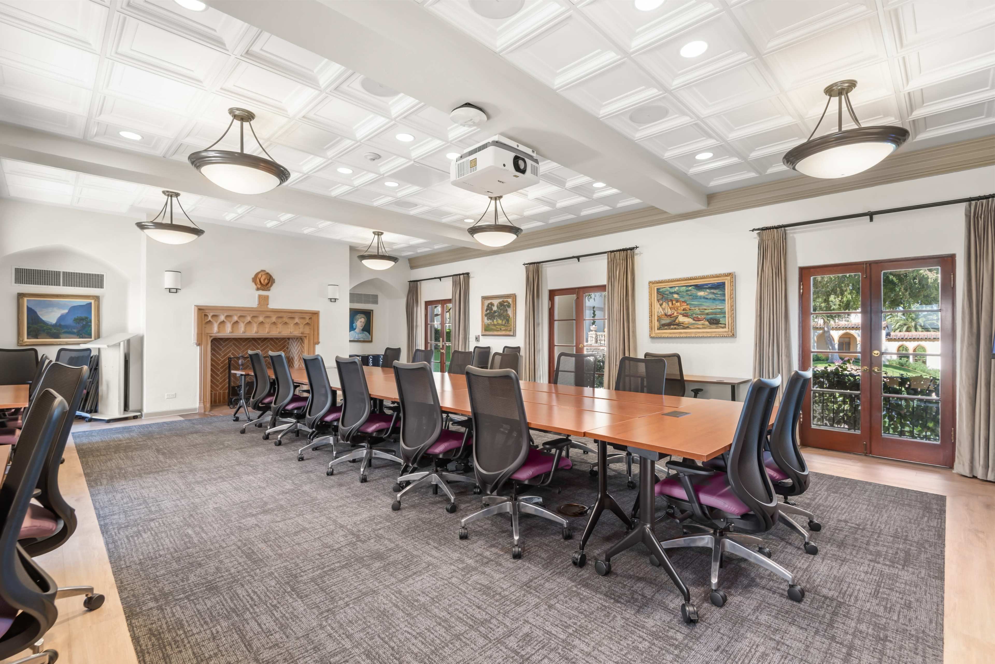 The image shows a modern conference room with a long table, ergonomic chairs, a projector, and artistic paintings on the walls.