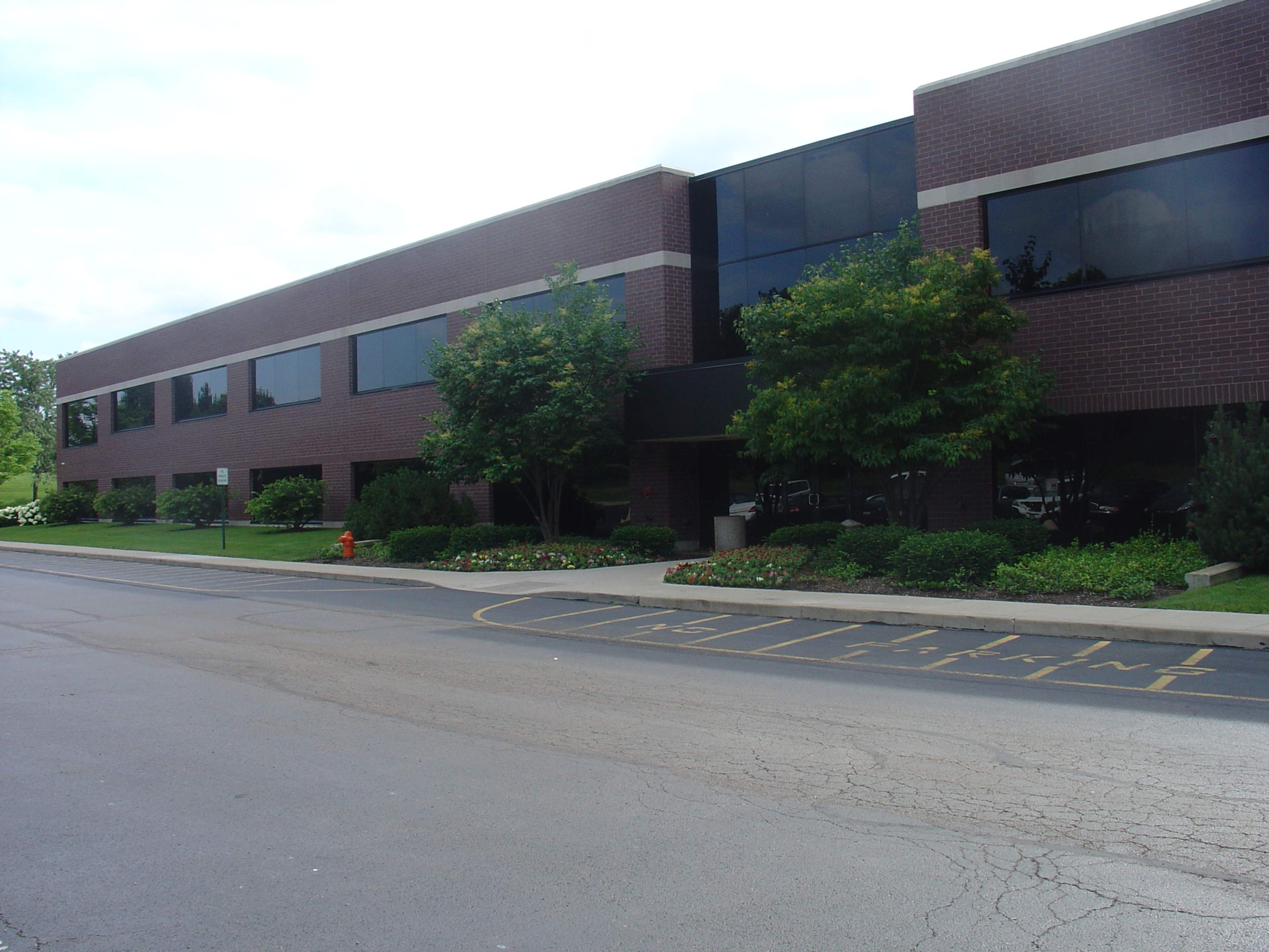 A modern brick office building with large windows and landscaped greenery in front.