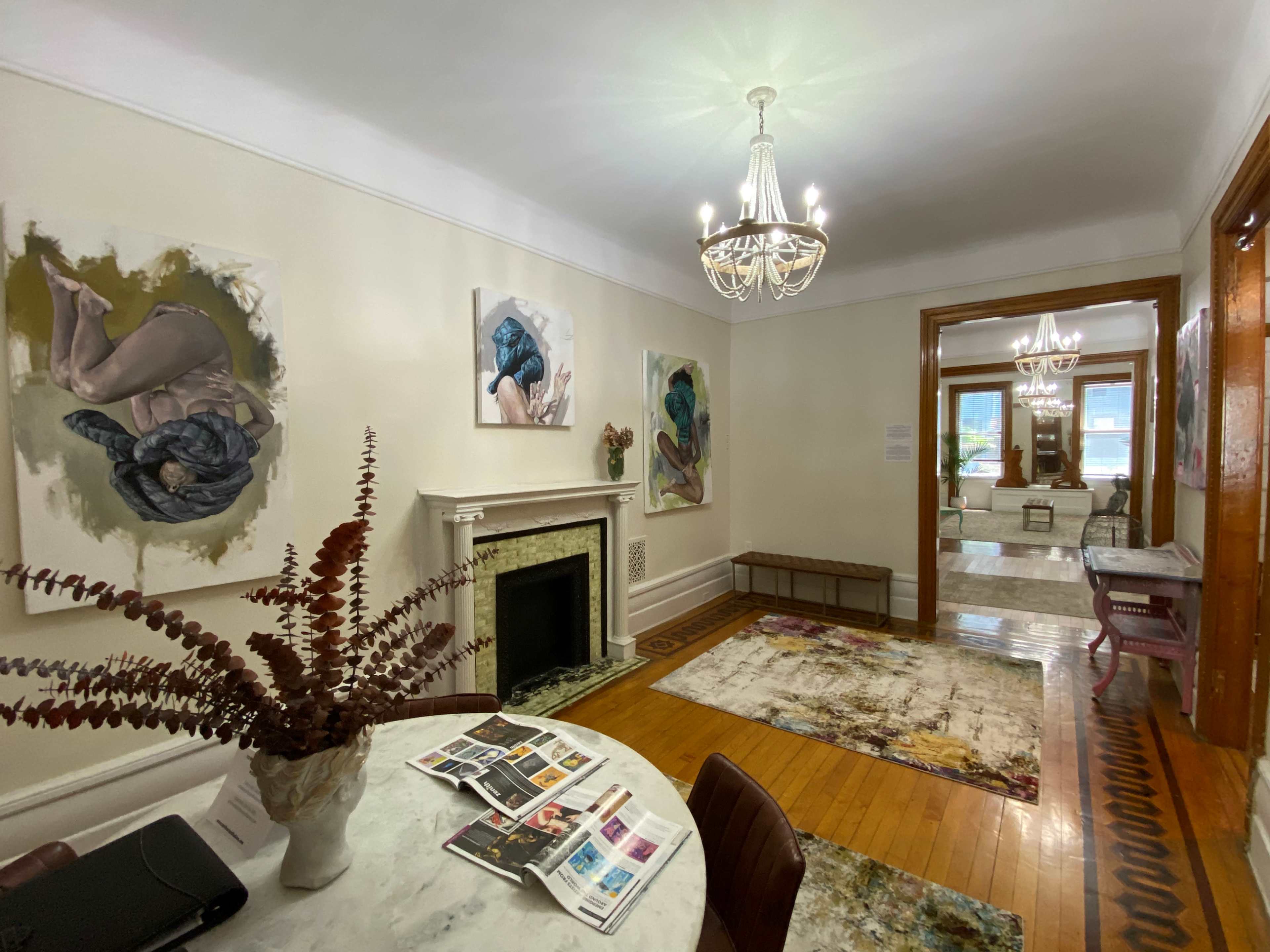 A well-lit hallway featuring a decorative marble table with art magazines, a fireplace, and several paintings on the walls.