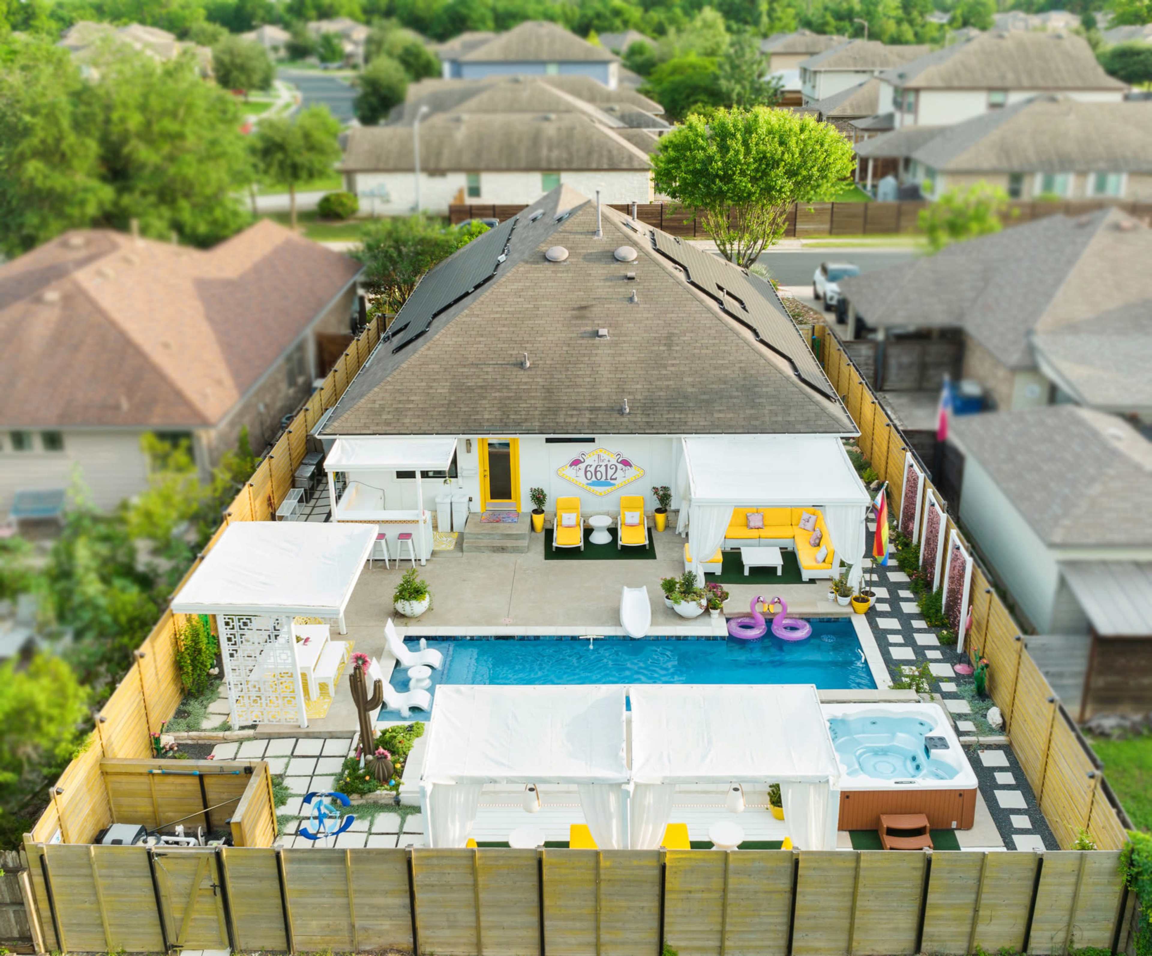 The image shows a backyard with a swimming pool, covered seating areas, and a house surrounded by a wooden fence, with nearby residential homes visible in the background.
