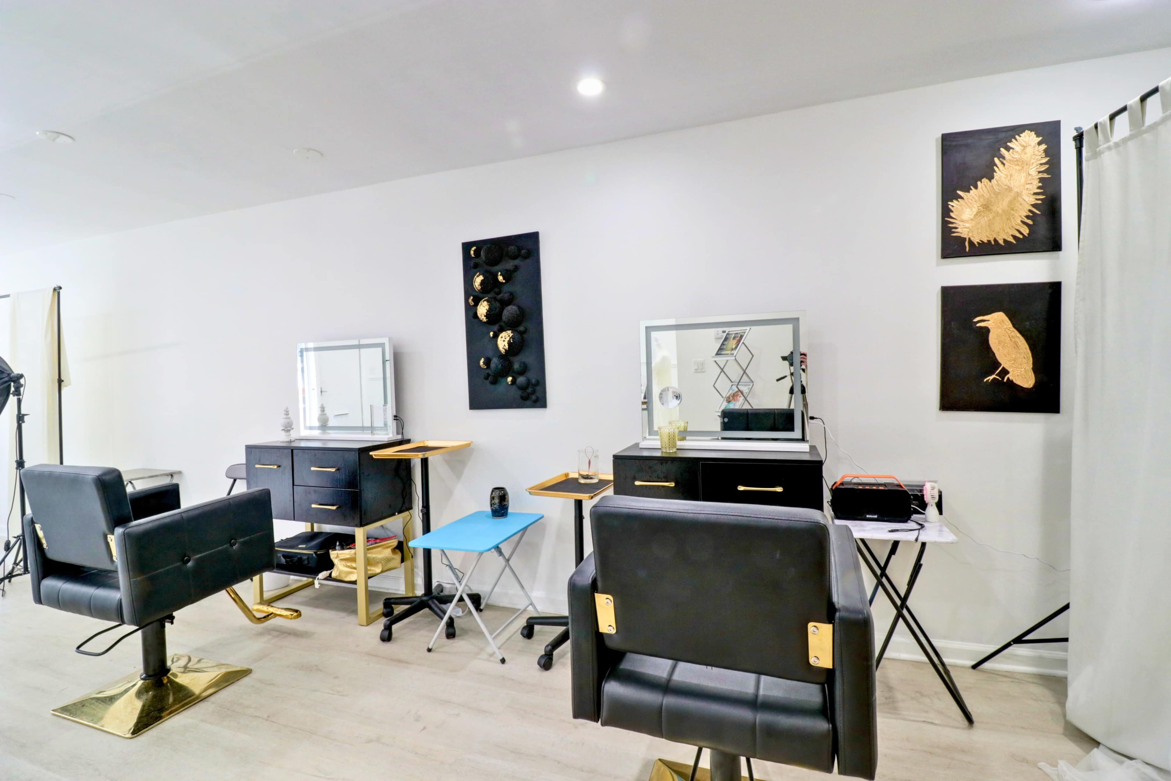 The image shows a modern hair salon with two black swivel chairs, several mirrors, and wall art, featuring gold and black accents.