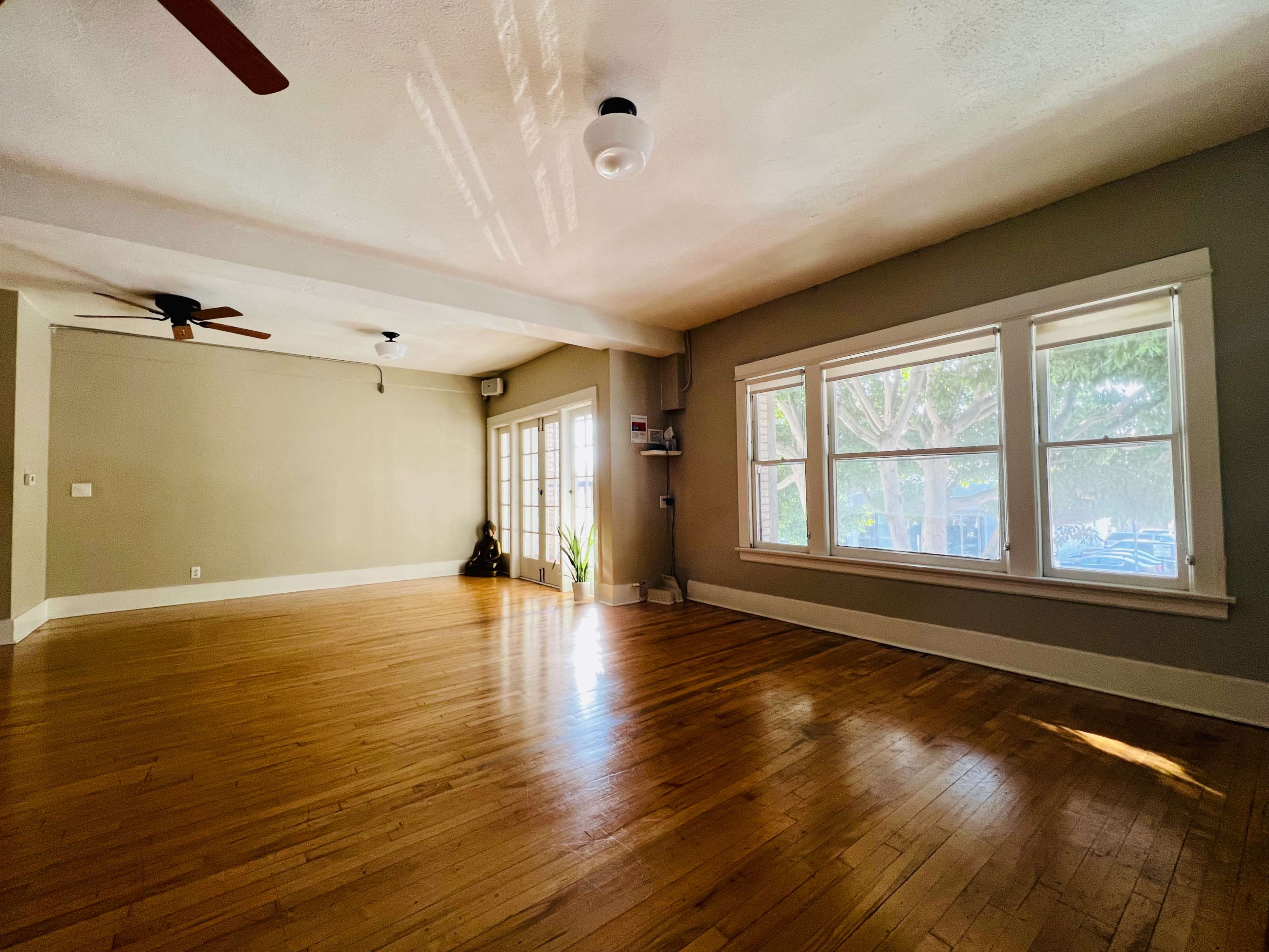 A spacious room with hardwood floors, large windows, and a set of French doors leading to an outdoor area.