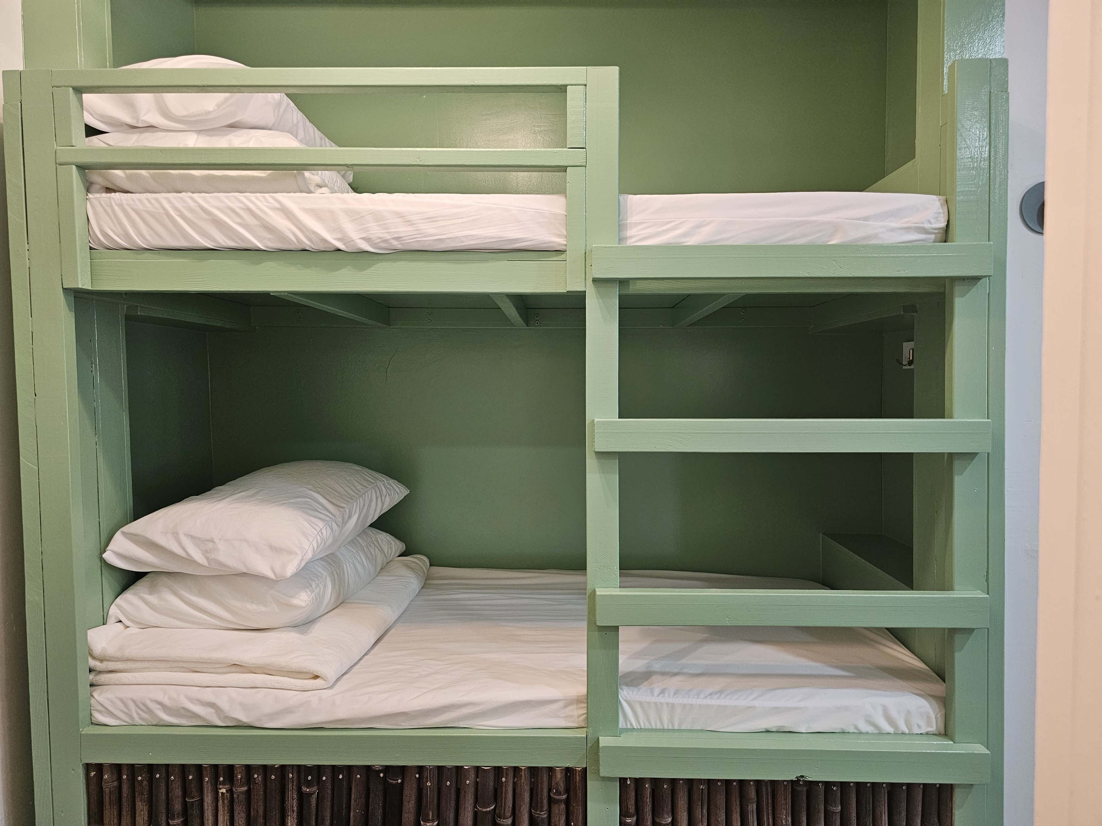 The image shows a green-walled bunk bed setup with two levels of beds made up with white linens.