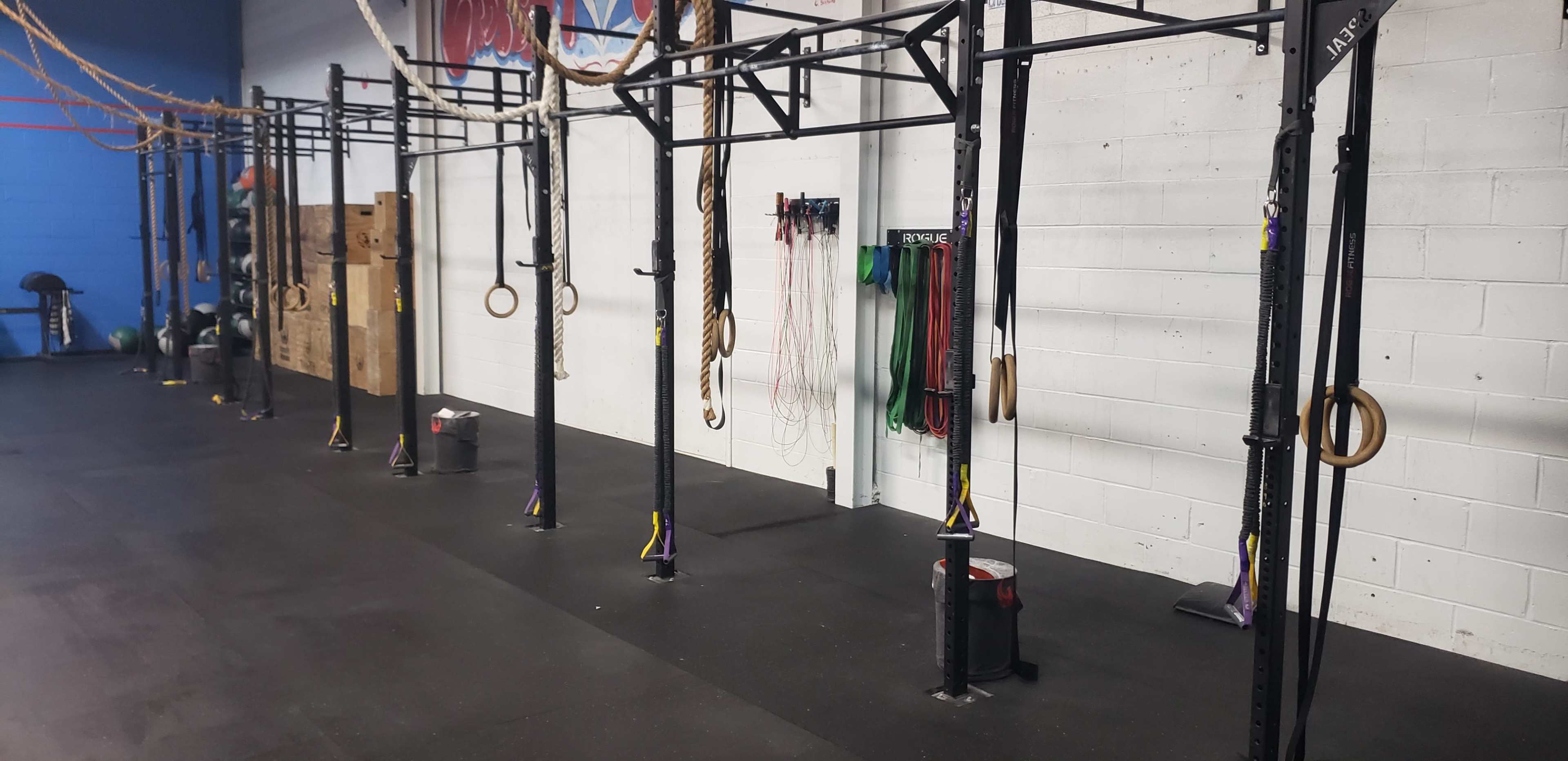 A gym space with multiple black metal rig structures equipped with various fitness accessories like ropes and rings against a white wall.